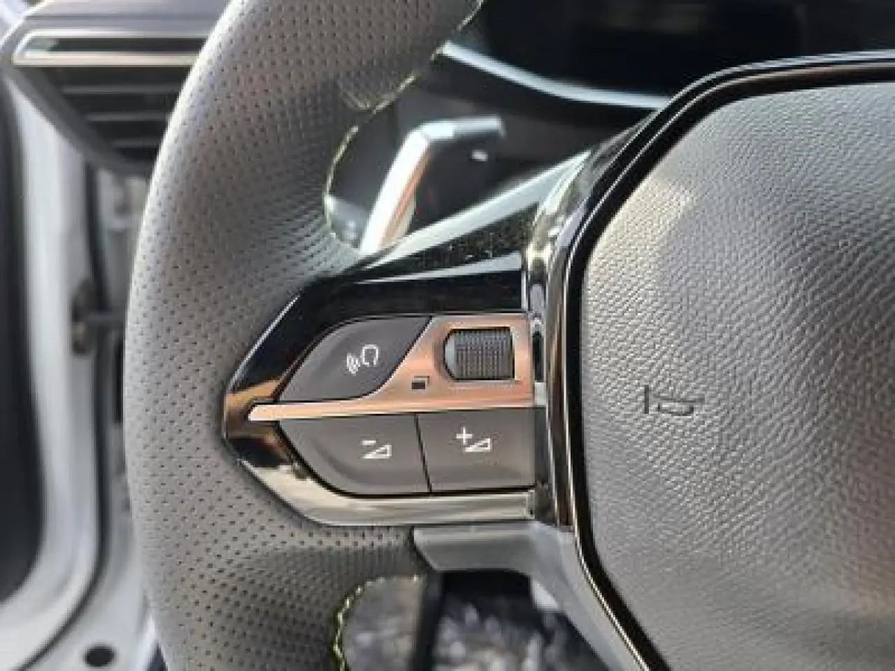 Gros plan sur les commandes gauche du volant cuir perforé de la Peugeot 2008 blanche toit noir, version hybride 2025.
