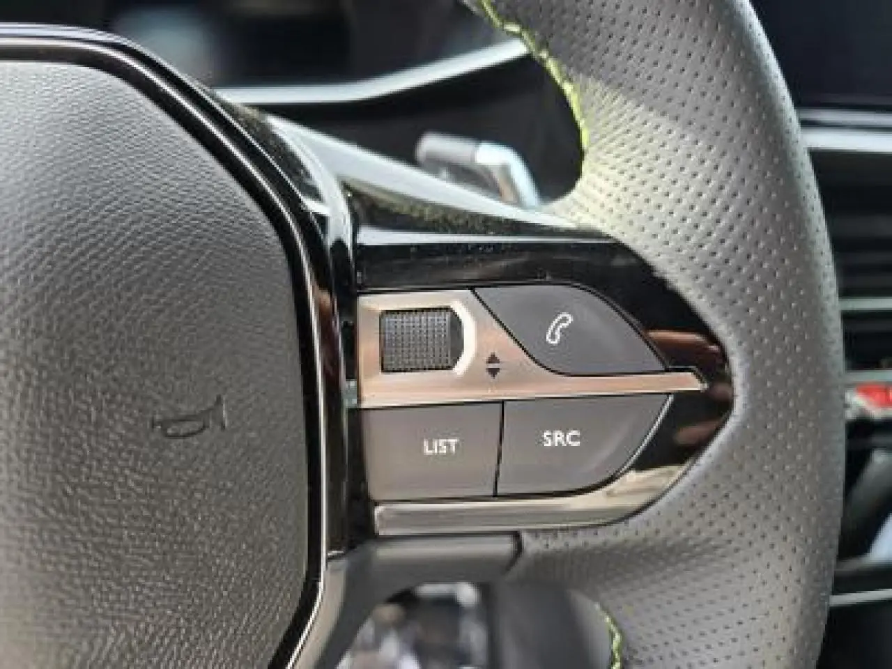 Gros plan sur les commandes gauche du volant cuir perforé du Peugeot 2008 blanc Okenite, version hybride 2025.