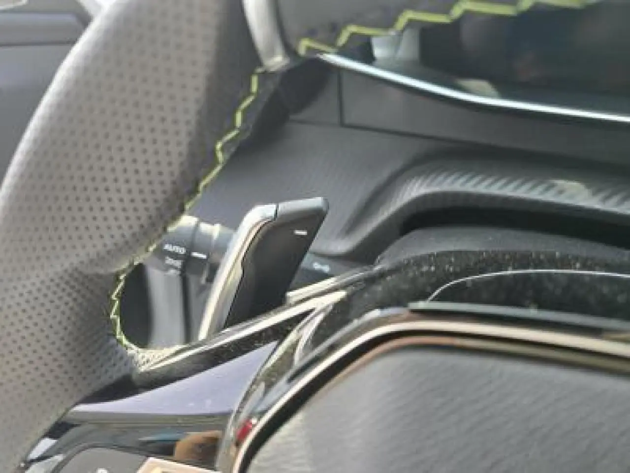 Gros plan sur le volant cuir perforé avec surpiqûres vertes et palettes de changement de vitesse du Peugeot 2008 hybride 2025.