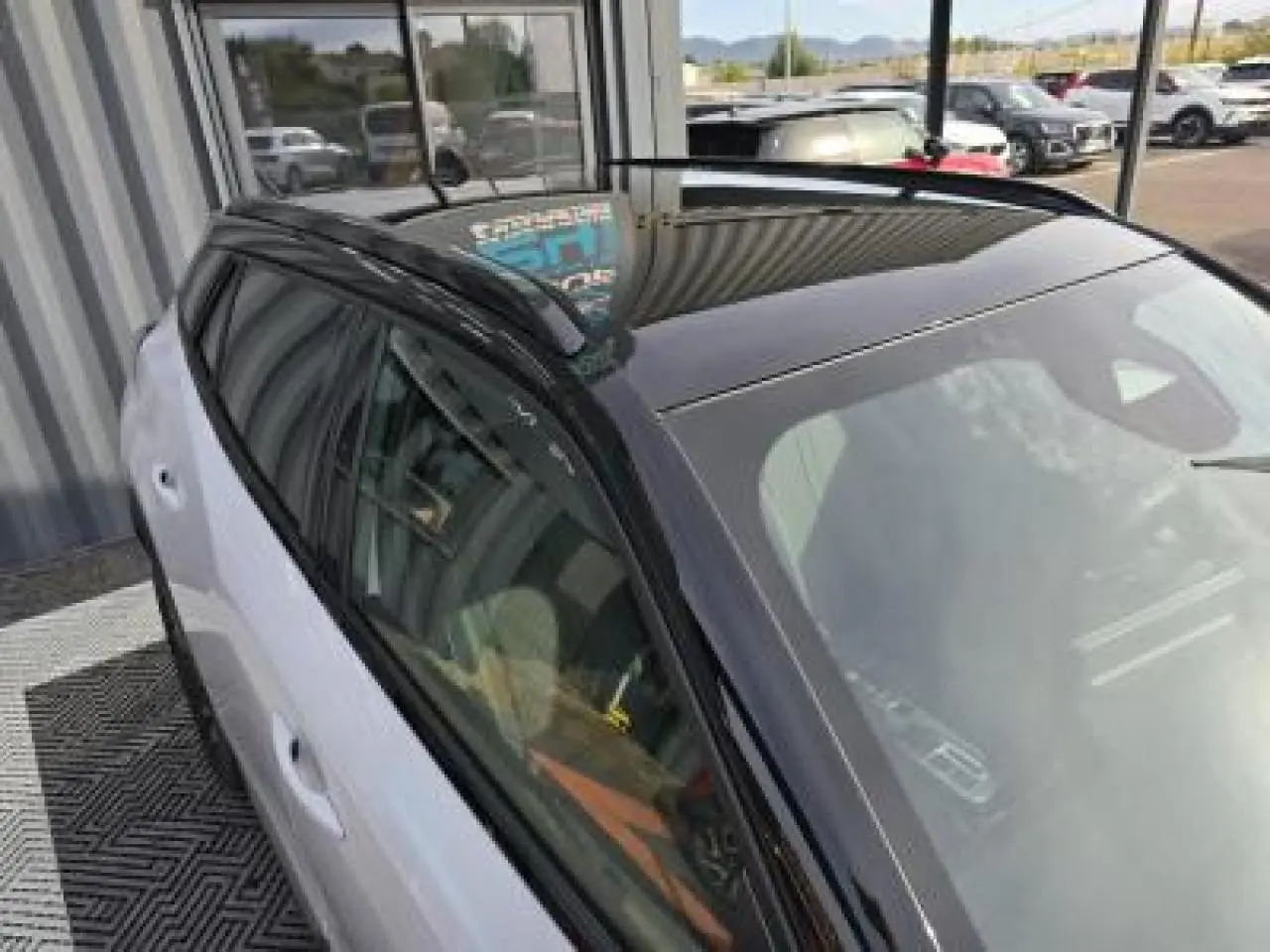 Peugeot 2008 hybride 2025 blanc Okenite toit noir en vue 3/4 arrière côté gauche avec barres de toit noires.