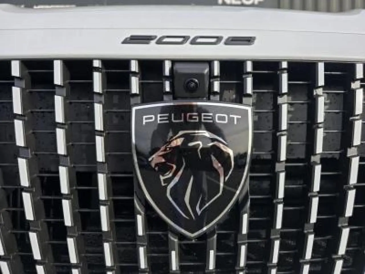 Gros plan sur la calandre noire brillante du Peugeot 2008 blanc Okenite avec logo lion et inscription 2008 au-dessus.