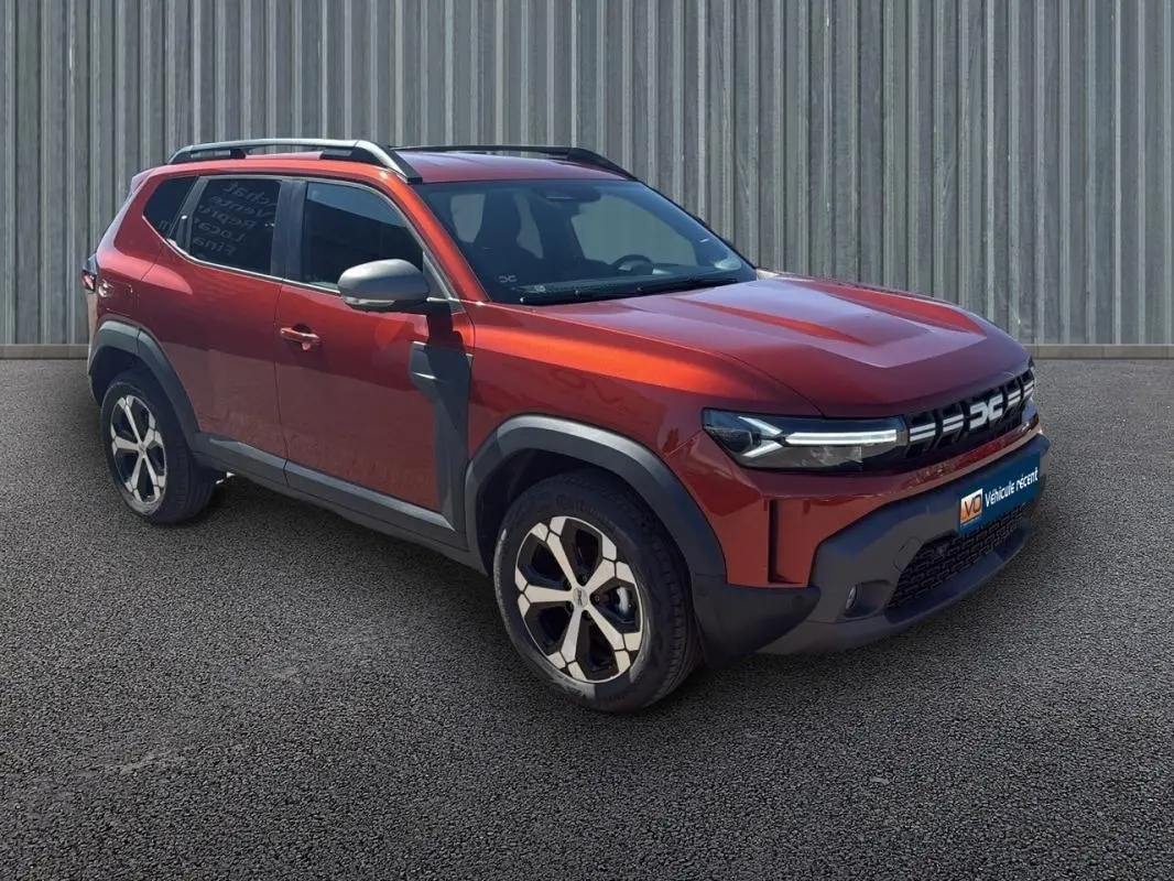 Vue 3/4 avant droit d'un Dacia Duster orange 2025 avec barres de toit et jantes alliage 18 pouces.