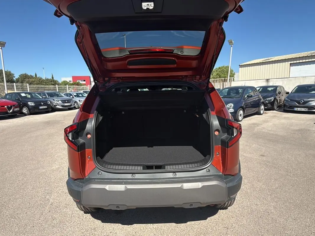 Vue arrière d'un Dacia Duster orange 2025 avec coffre ouvert, soulignant l'espace de chargement et les feux arrière distinctifs.