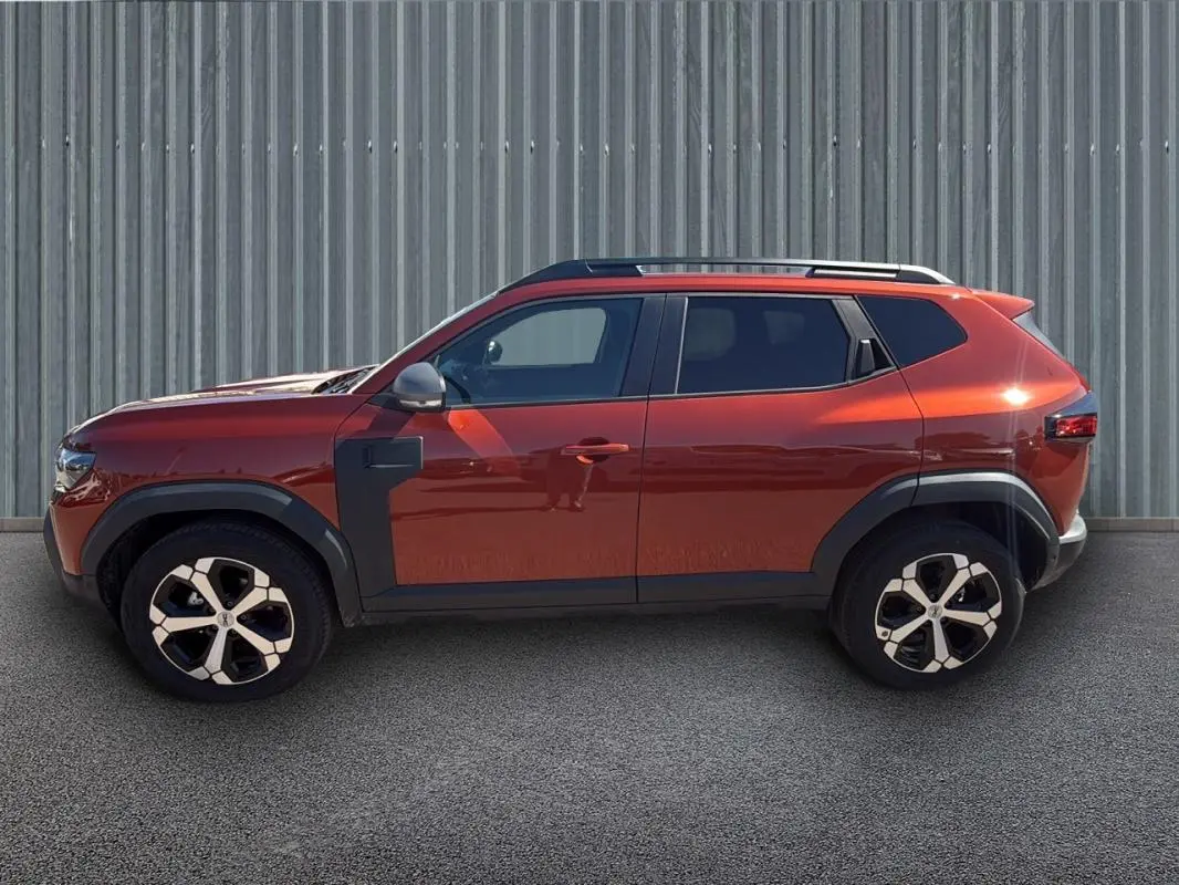 Profil côté gauche du Dacia Duster 2025 orange avec barres de toit et jantes alliage 18 pouces.