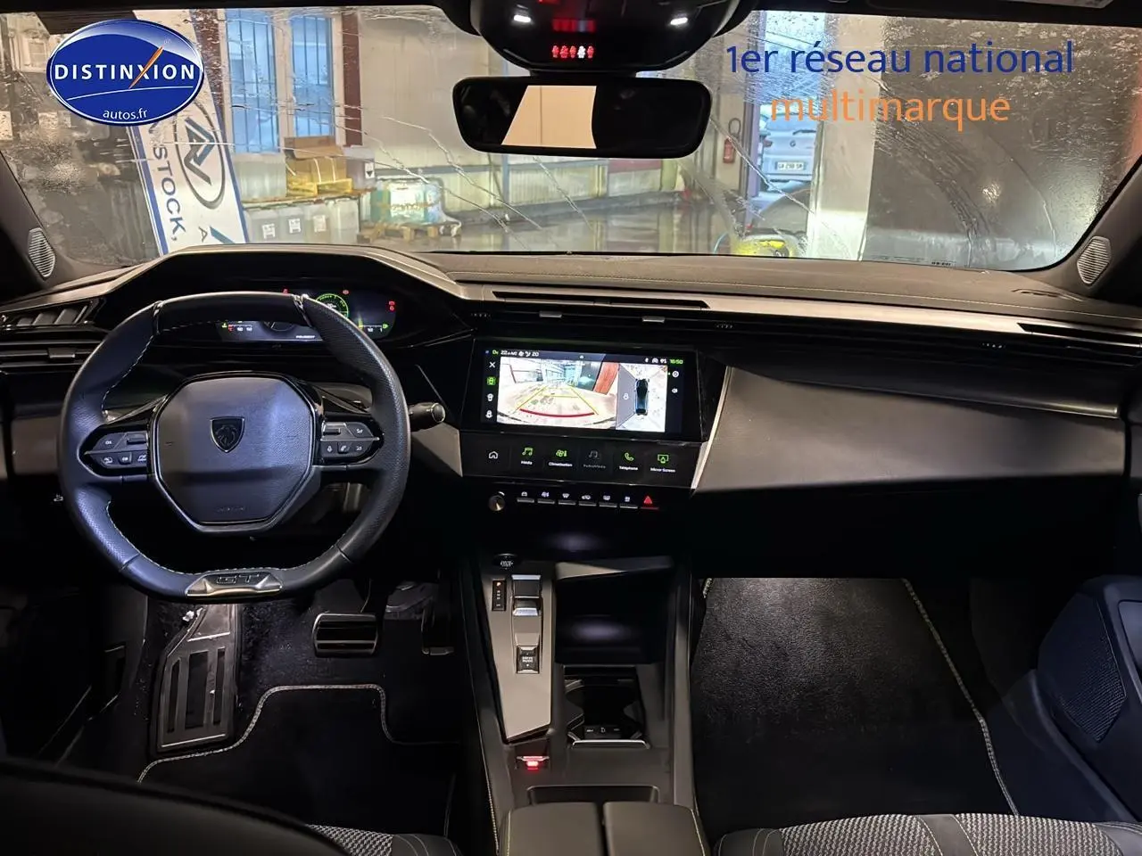 Vue intérieure avant du tableau de bord et volant cuir noir de la Peugeot 408 Hybrid 145 GT gris sélénite, écran tactile allumé.