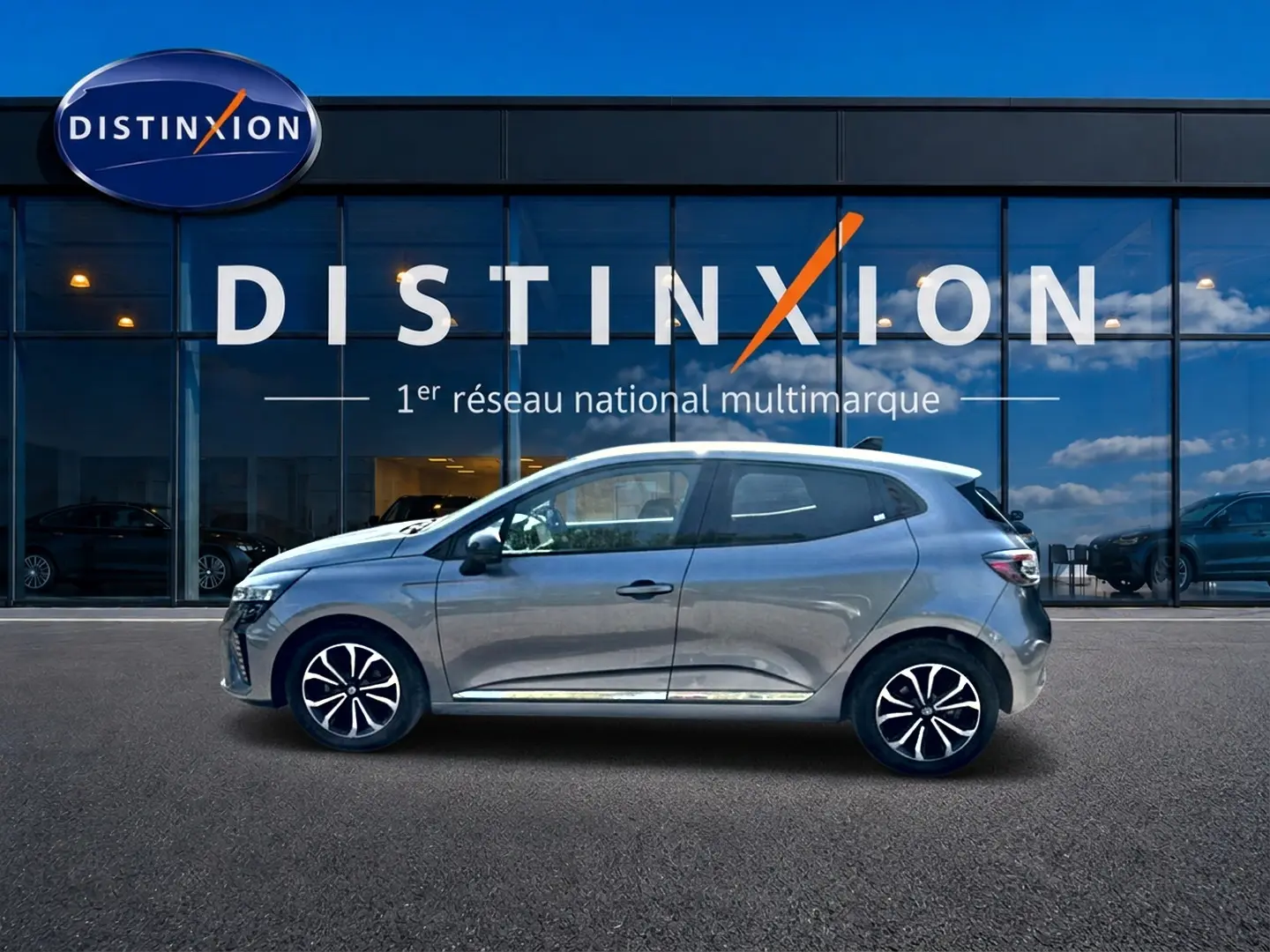 Profil côté gauche de la Renault Clio V gris schiste 2025, avec jantes alu et vitres surteintées devant un showroom Distinxion.