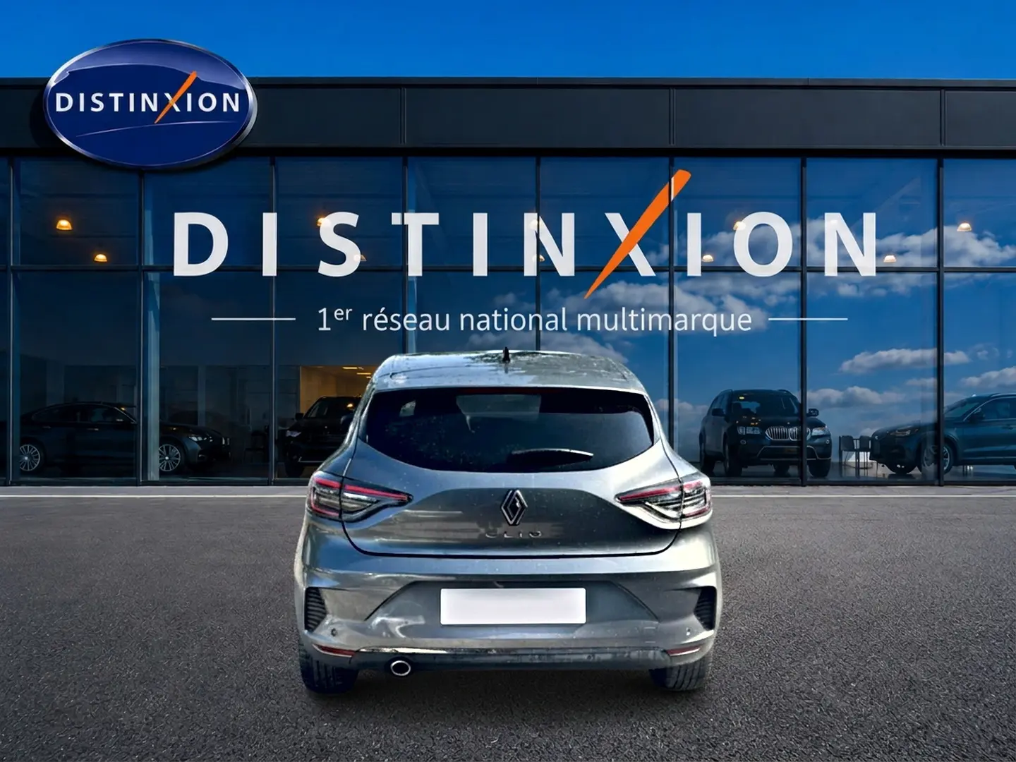 Vue arrière d'une Renault Clio V gris schiste garée devant une vitrine avec logo Distinxion.