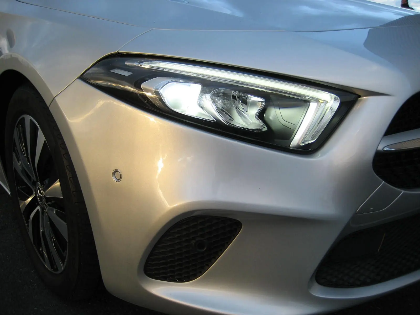 Gros plan sur l'avant droit gris d'une Mercedes Classe A 180d 2021, mettant en valeur le phare LED et la calandre.