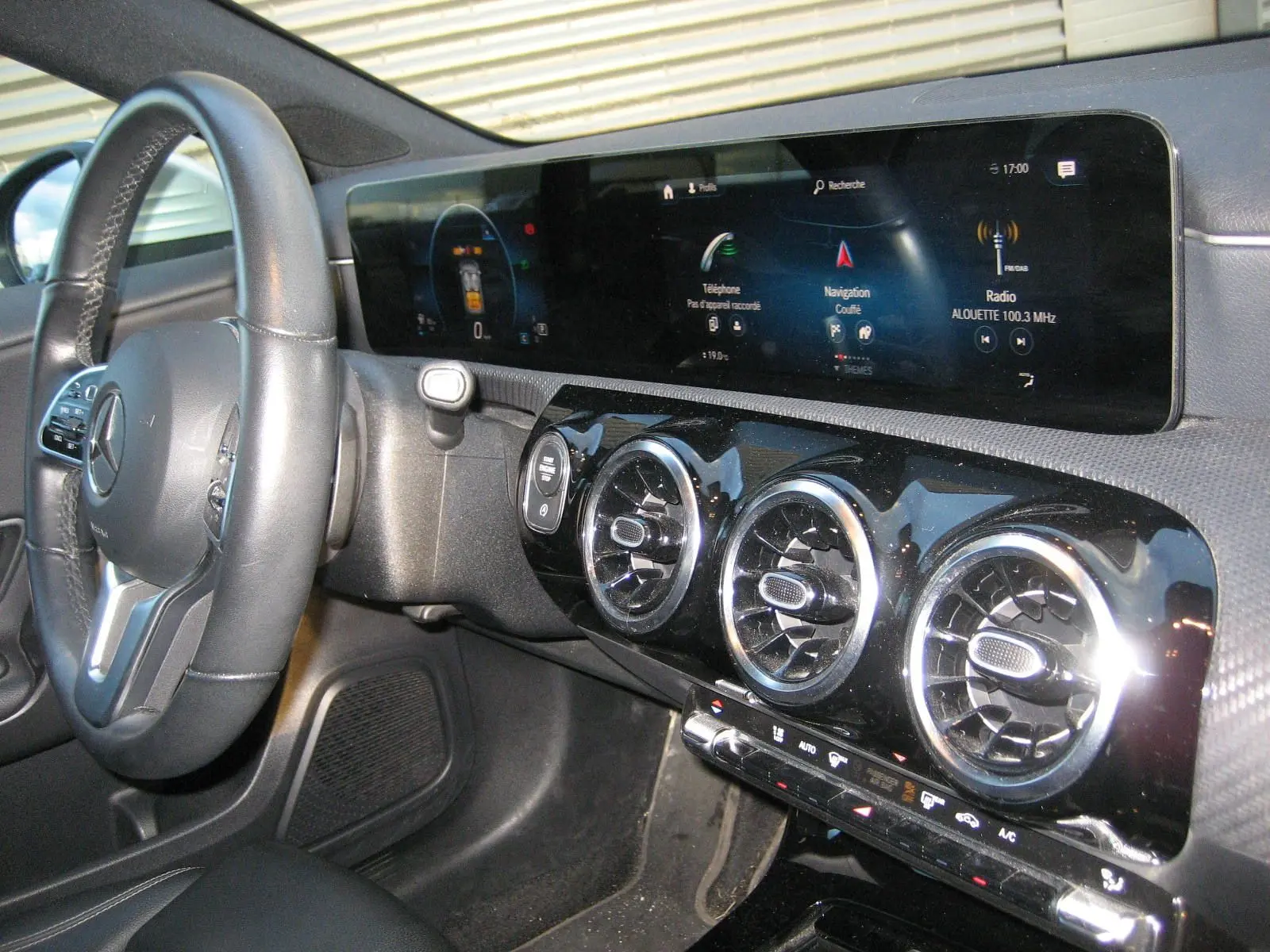 Vue intérieure côté conducteur de la Mercedes Classe A 180d 2021, tableau de bord noir avec écran tactile panoramique et aérateurs ronds chromés.