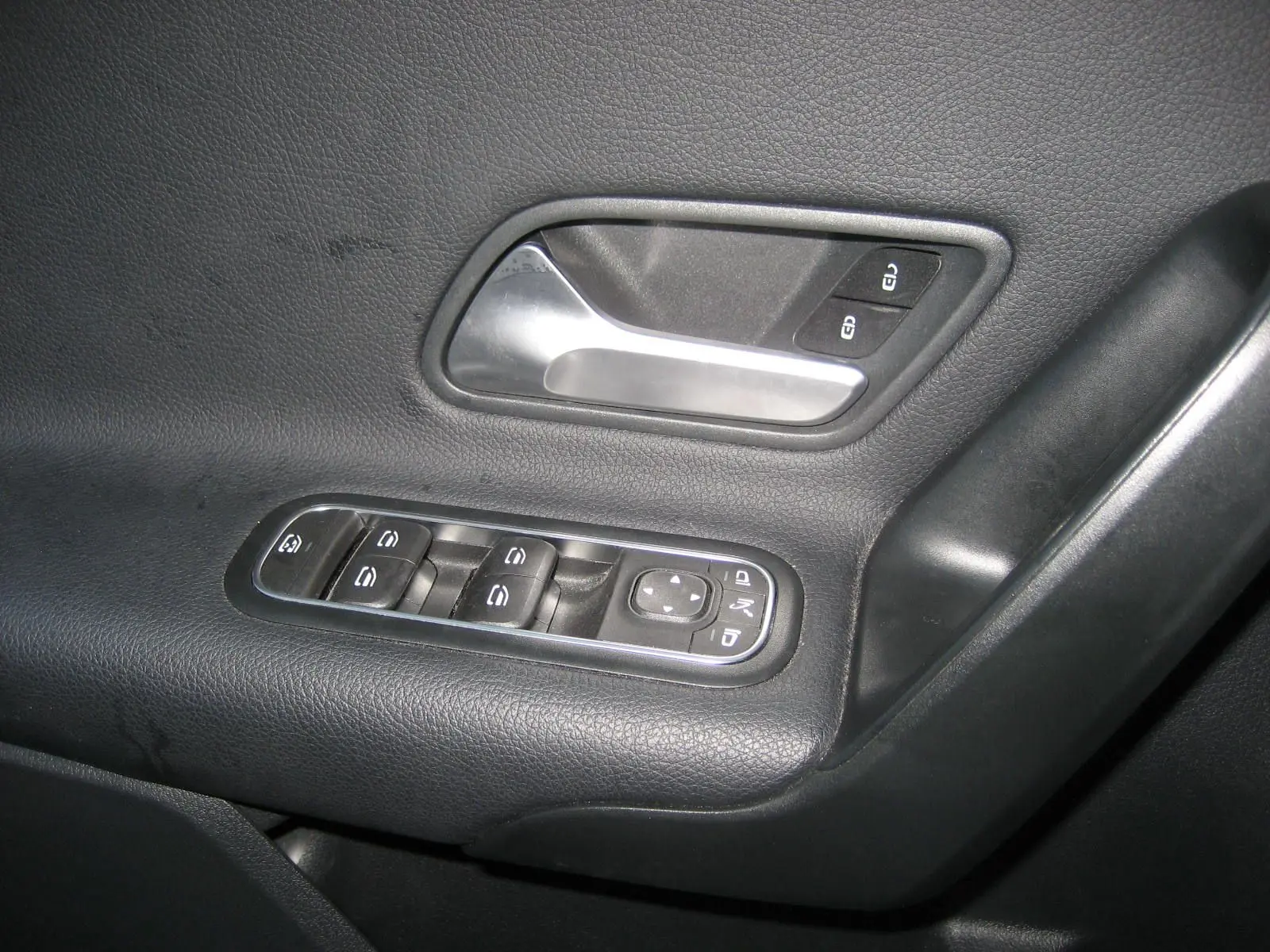Gros plan sur la poignée intérieure et les commandes des vitres côté gauche d'une Mercedes Classe A gris foncé.