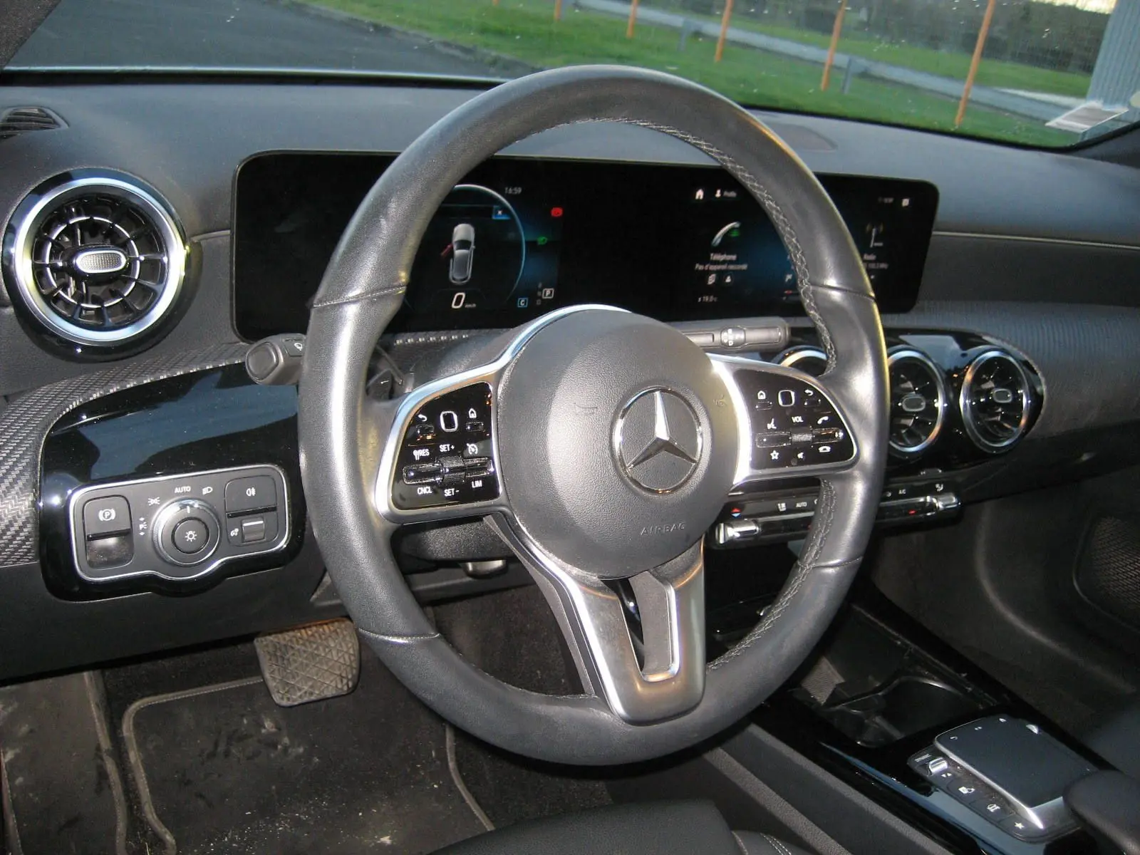 Vue intérieure centrée sur le volant cuir noir d'une Mercedes Classe A 180d 2021 avec tableau de bord numérique.