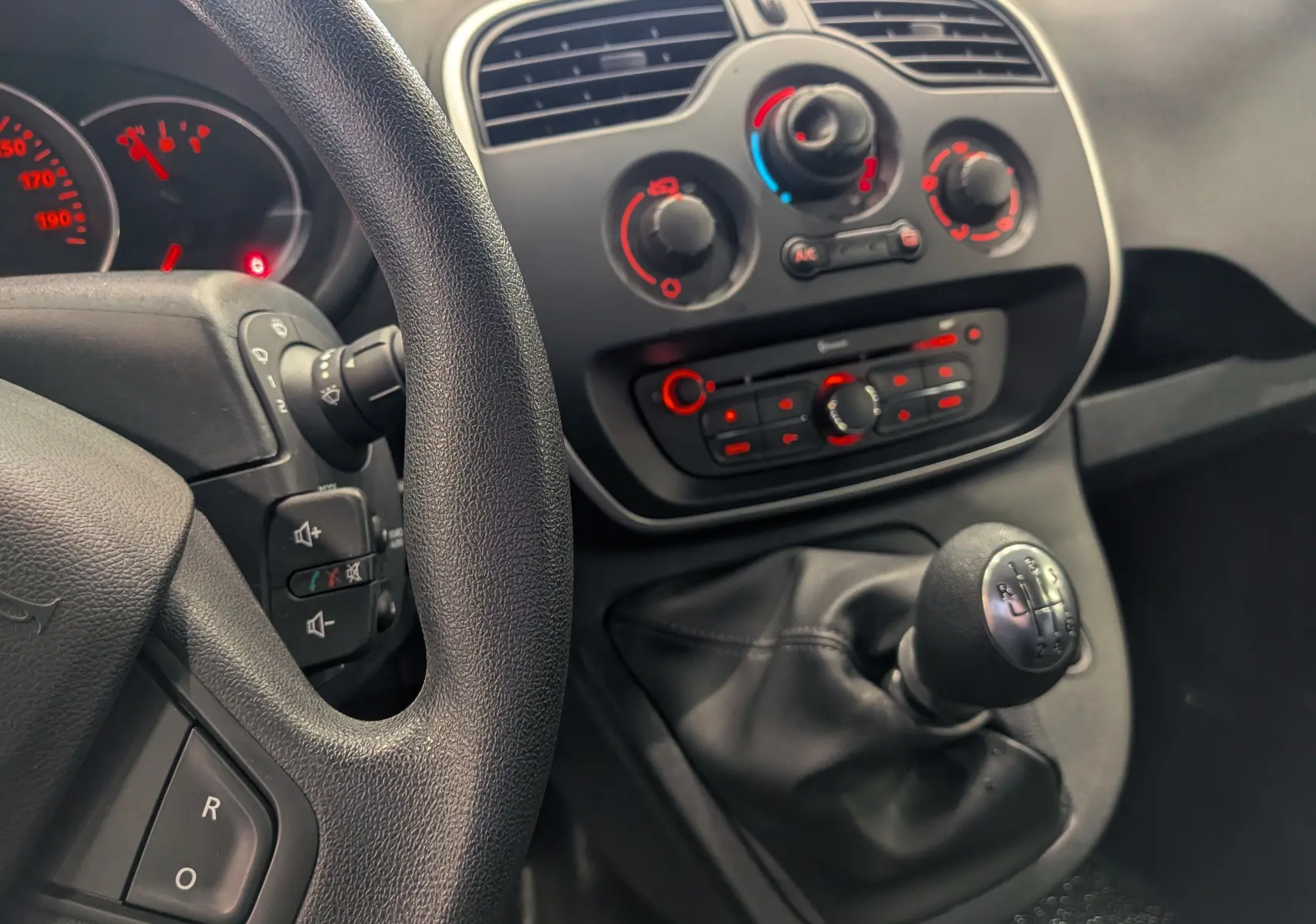 Vue intérieure centrée sur la console centrale et levier de vitesse d’un Renault Kangoo Express blanc, avec tableau de bord et commandes climatisation visibles.
