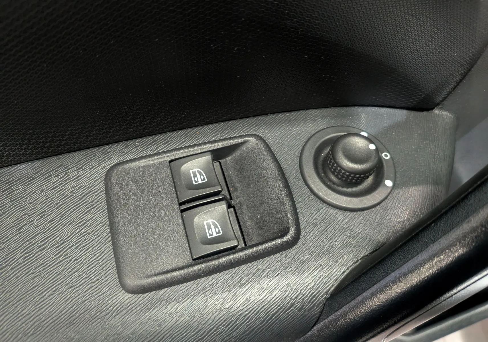 Gros plan sur les commandes des vitres électriques et le réglage des rétroviseurs côté conducteur du Renault Kangoo Express blanc.