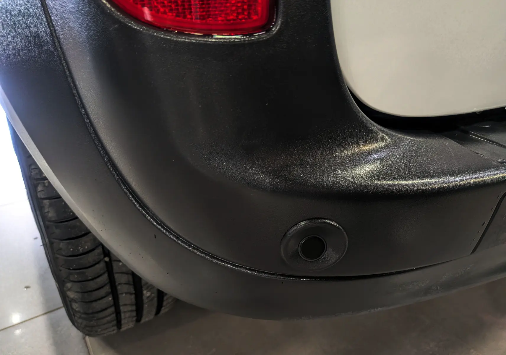 Gros plan sur le pare-chocs arrière droit blanc minéral du Renault Kangoo Express avec capteur de recul visible.