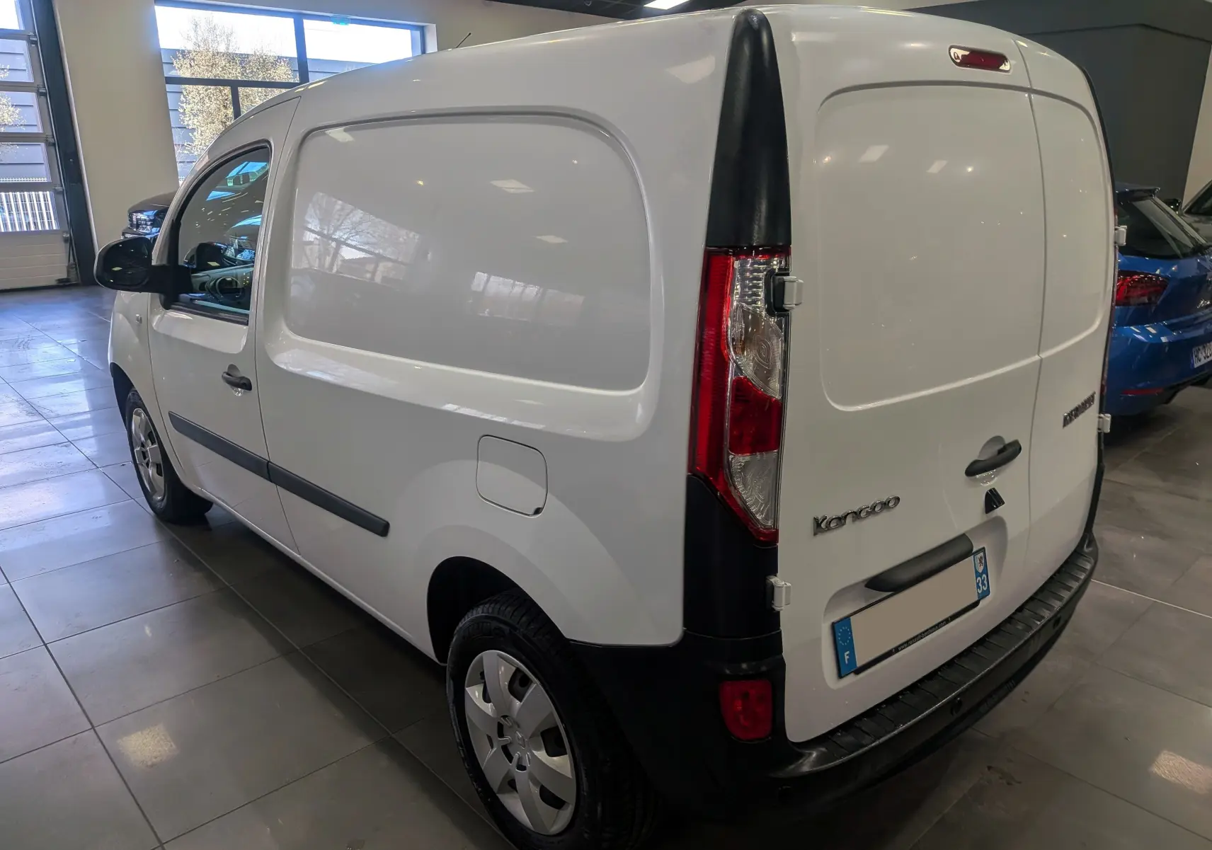 Vue 3/4 arrière droite du Renault Kangoo Express blanc minéral, fourgon utilitaire avec portes arrière pleines en intérieur showroom.
