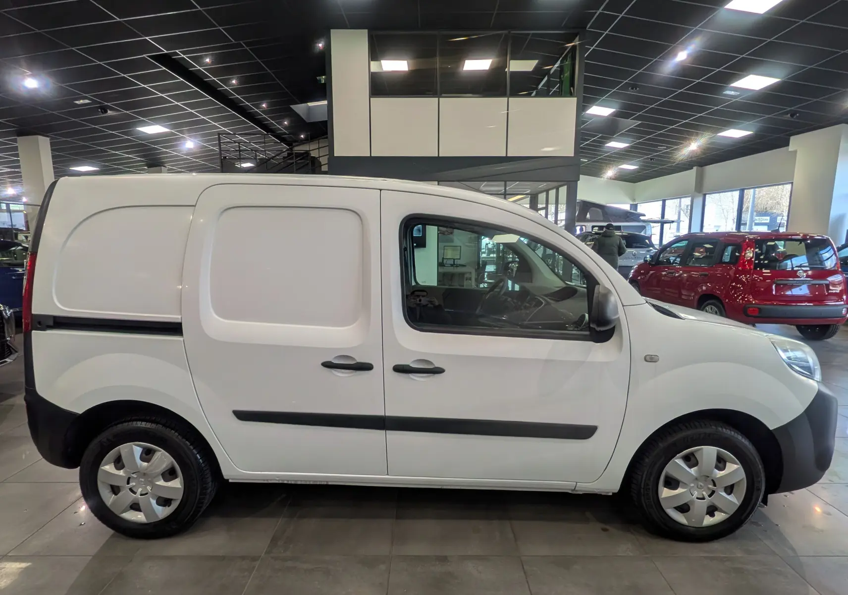 Vue de profil côté gauche d'un Renault Kangoo Express blanc Minéral, utilitaire compact en showroom lumineux.