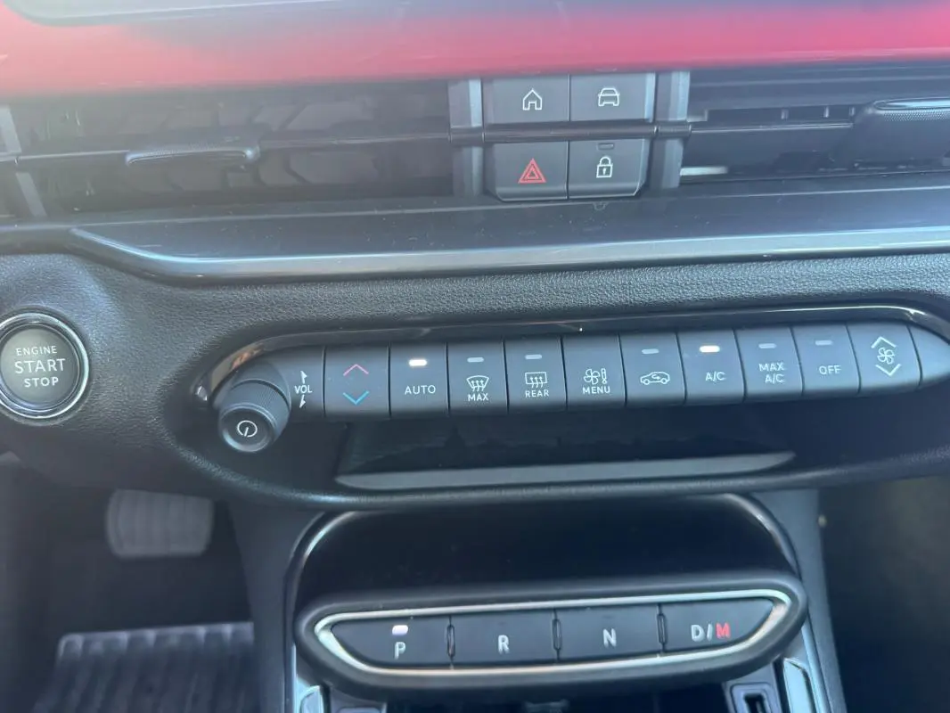 Vue intérieure centrée sur la console centrale du Fiat 600 rouge 2025, montrant les commandes climatisation et boîte auto.