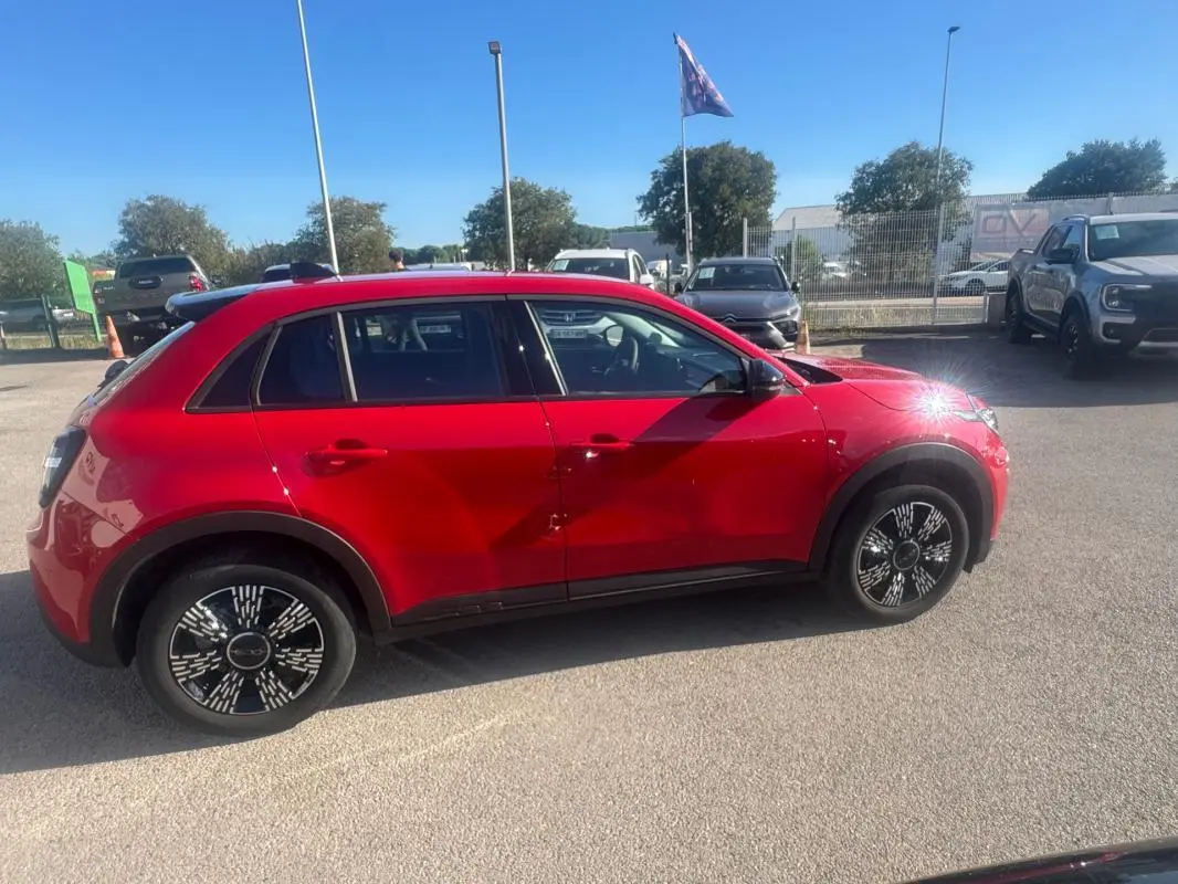 Vue de profil côté gauche d'une FIAT 600 T-Gen 3 rouge 2025 avec jantes noires au design graphique, stationnée en extérieur.