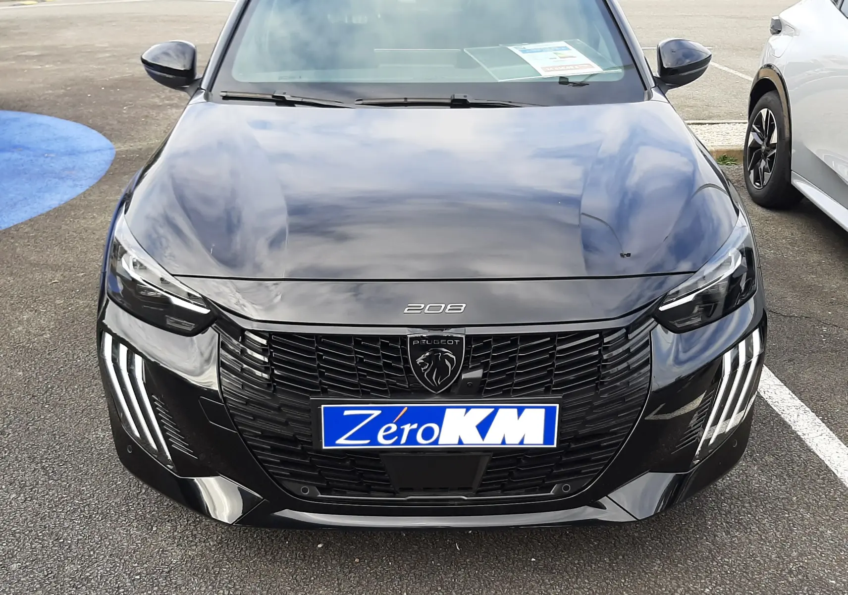 Vue avant d'une Peugeot 208 Hybrid 145ch GT noire perla avec feux LED distinctifs et plaque Zéro KM.