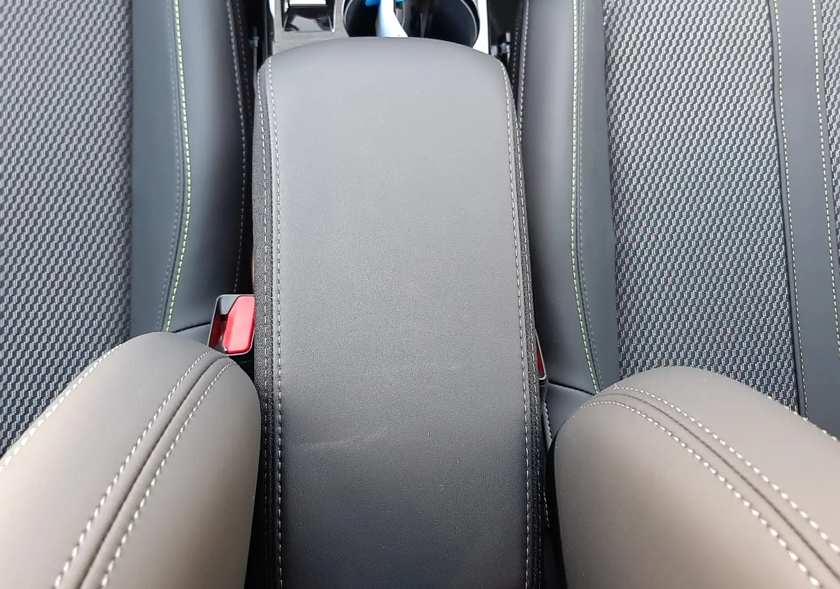 Vue plongeante sur l'accoudoir central noir et les sièges avant en tissu et cuir du Peugeot 208 Hybrid 145ch GT 2026.