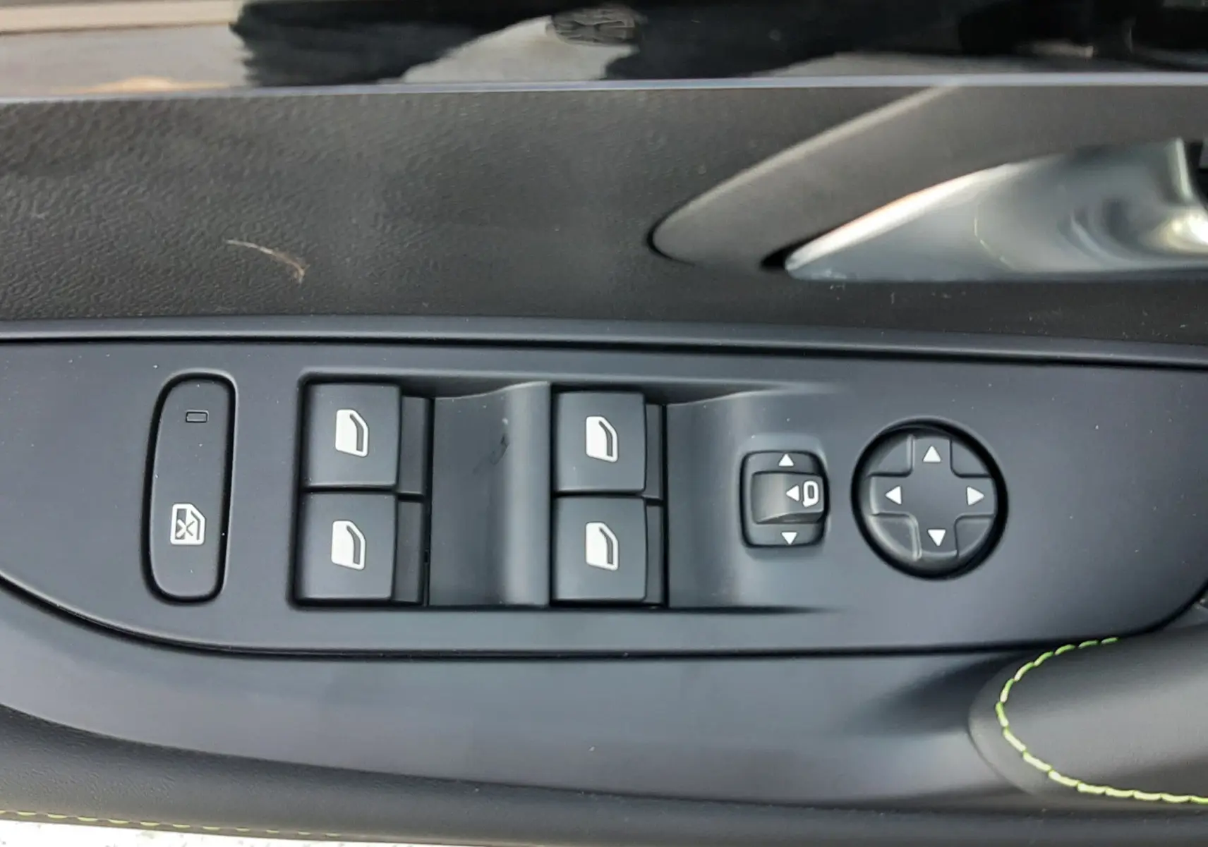 Gros plan sur la commande des vitres et rétroviseurs côté conducteur d’une Peugeot 208 noire Perla, avec surpiqûres vertes.