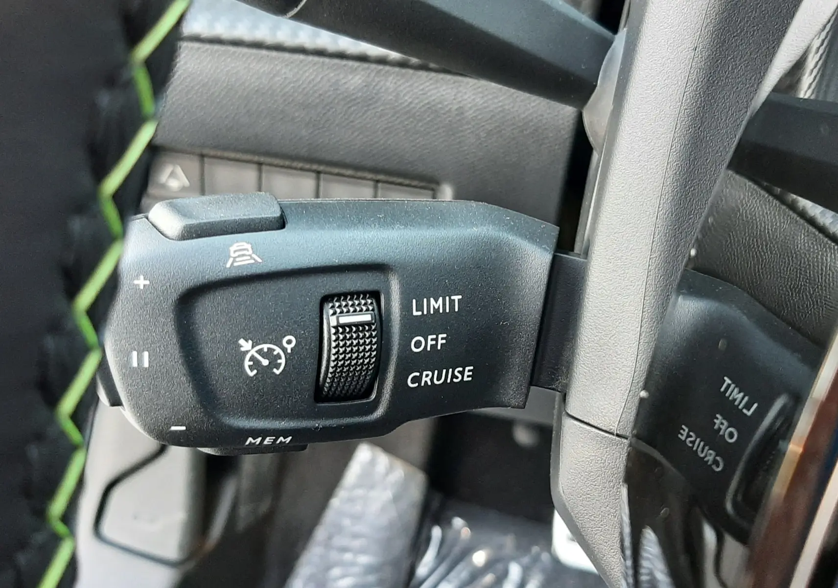 Gros plan sur la commande de régulateur de vitesse noire avec marquages blancs, sur le volant du Peugeot 208 Hybrid 145ch GT.