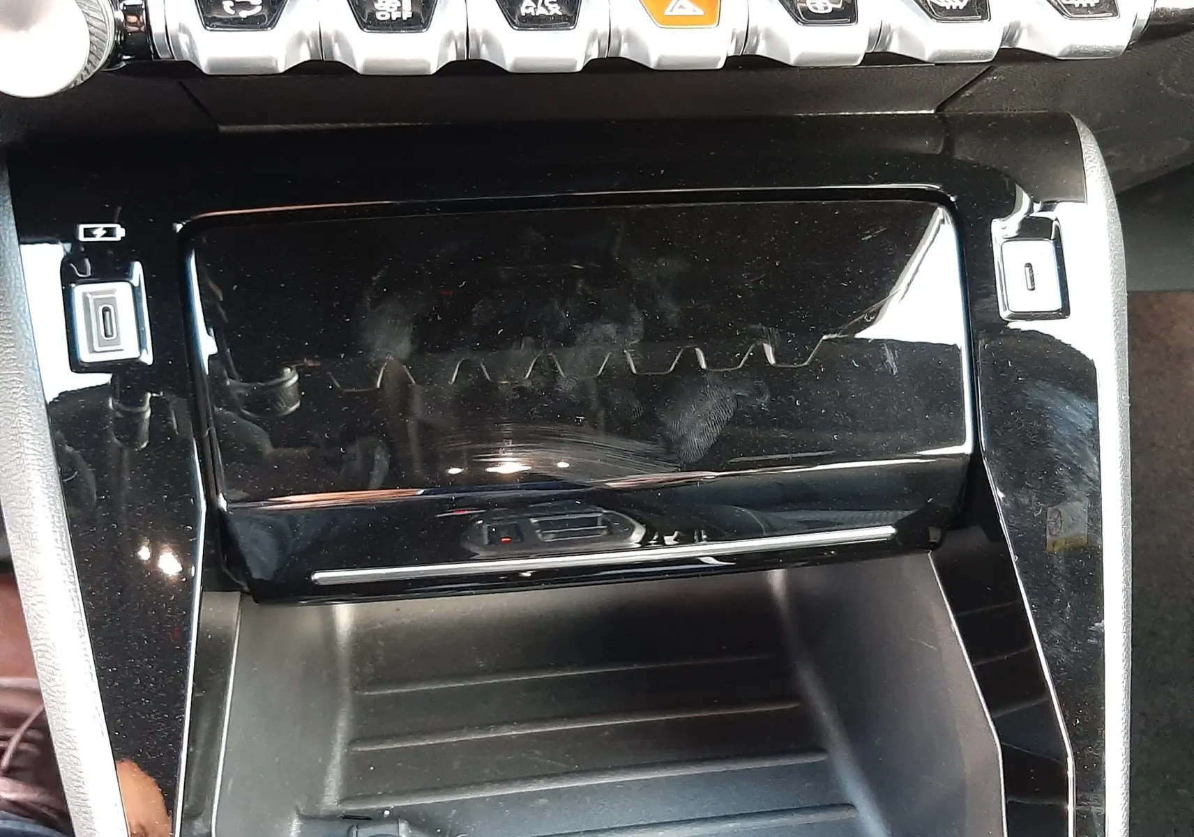 Vue rapprochée de la console centrale noire brillante du Peugeot 208 Hybrid 145CH GT avec boutons de commande et prise 12V.