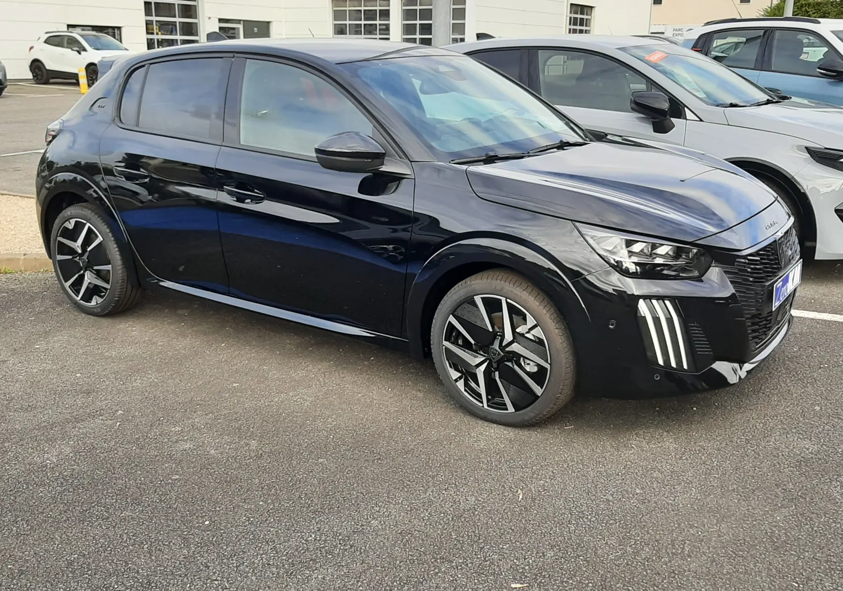 Peugeot 208 Hybrid 145ch GT noire perla en 3/4 avant droit, avec feux LED verticaux distinctifs et jantes bi-ton.