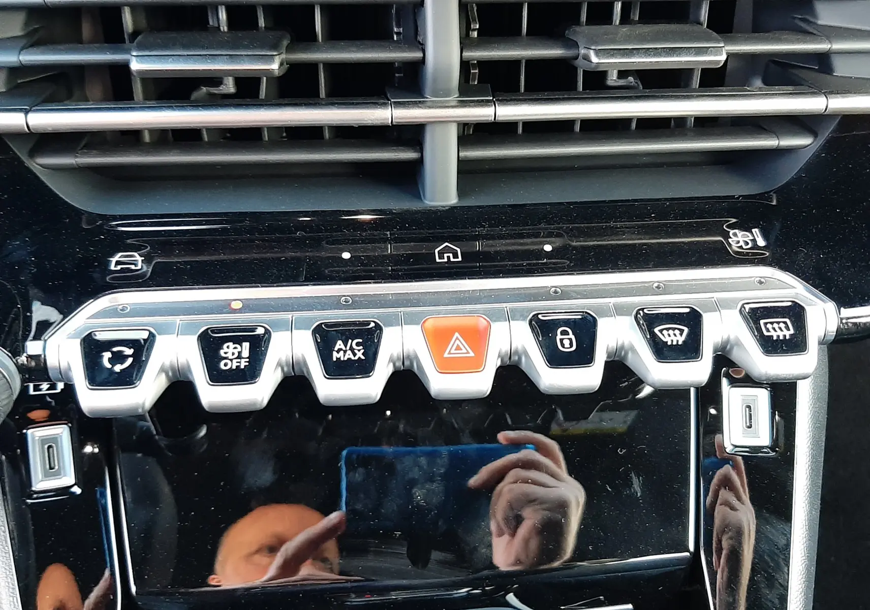 Gros plan sur la console centrale noire perla de la Peugeot 208 Hybrid 145ch GT, avec boutons de commande et aérateurs.