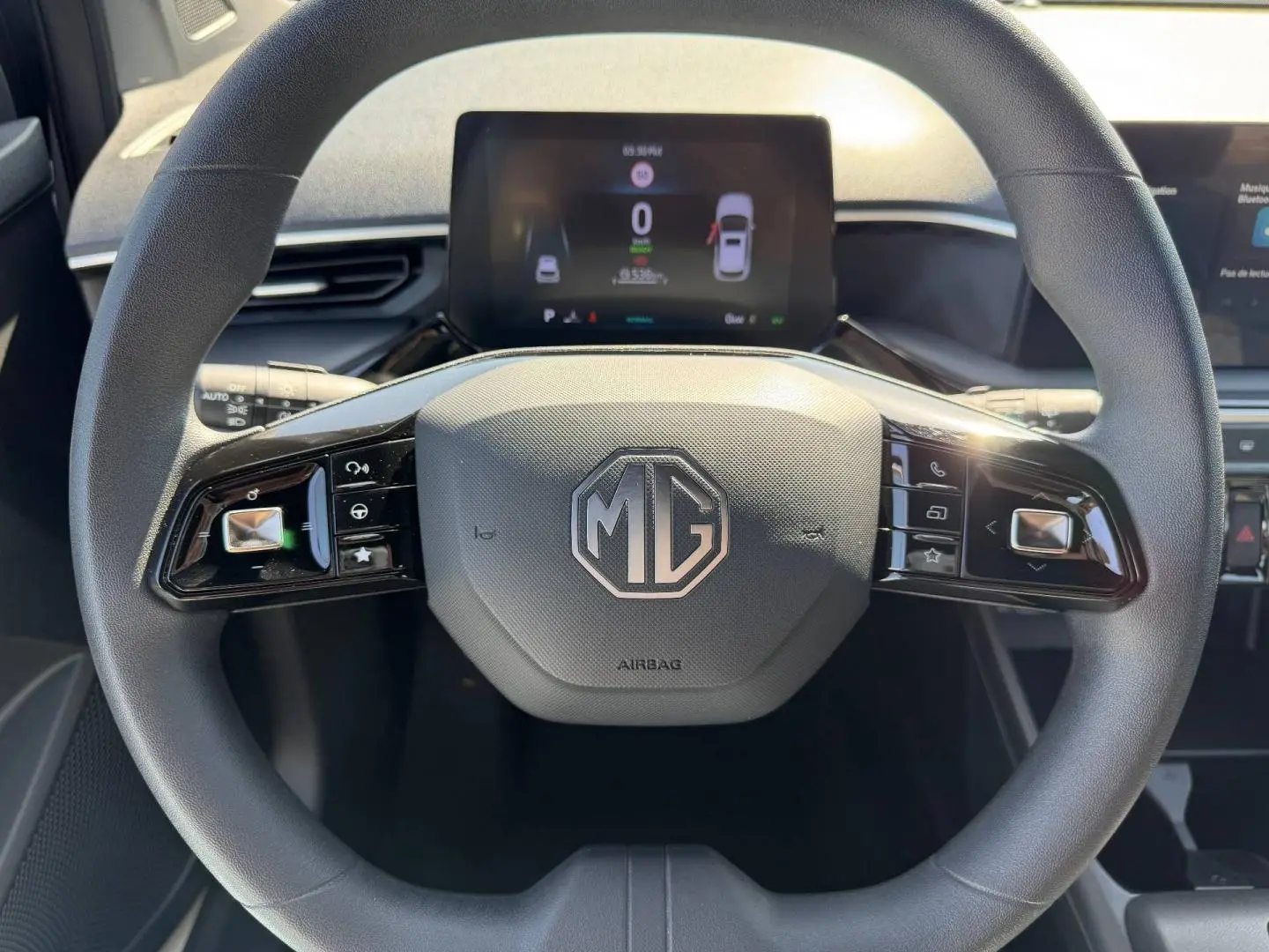Vue rapprochée du volant noir de la MG3 1.5 Hybrid+ 195ch Comfort avec logo MG et écran numérique en arrière-plan.