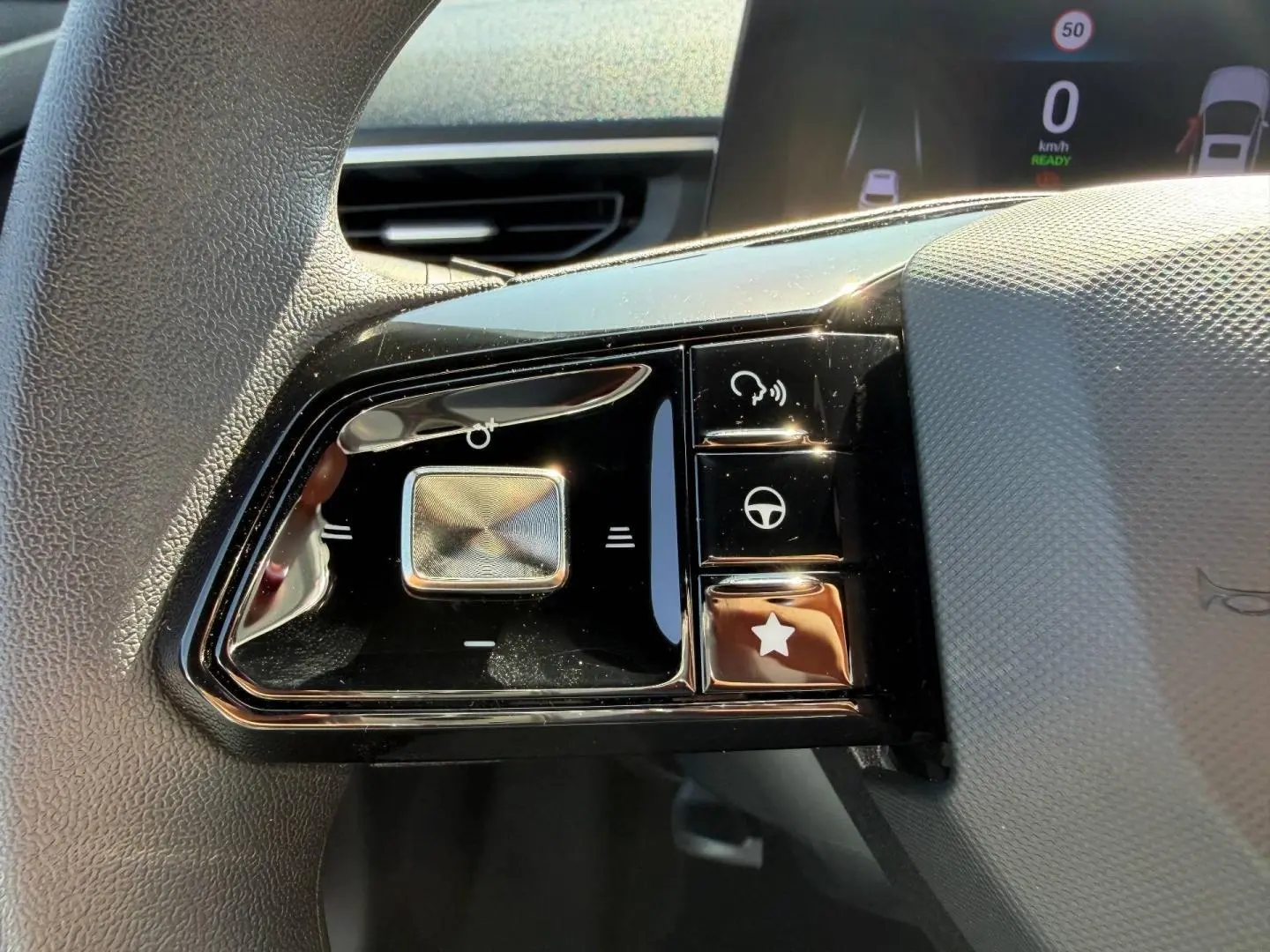 Gros plan sur les commandes noires du volant côté gauche du MG3 blanc hybride 2025 avec écran numérique en arrière-plan.