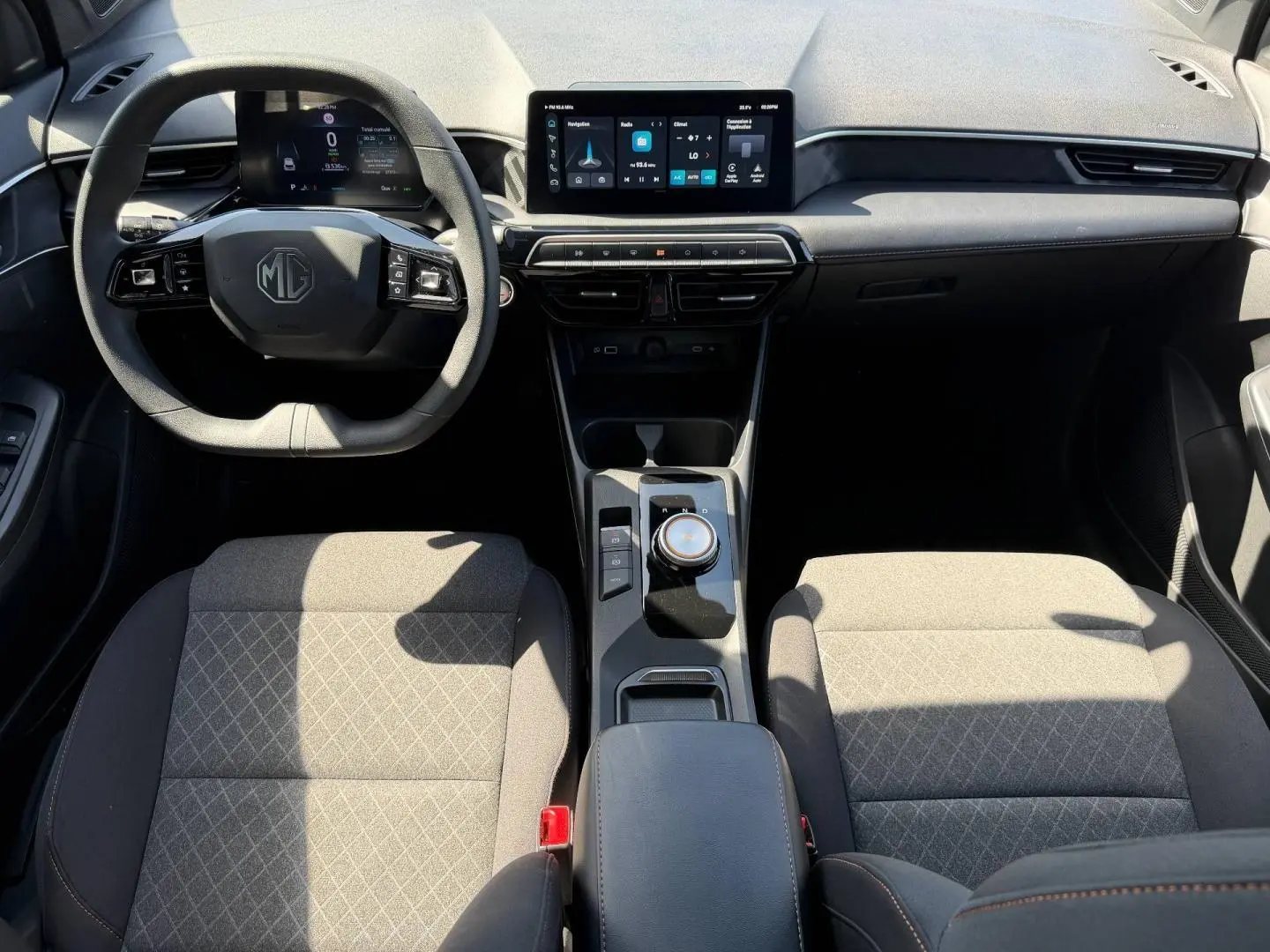 Vue intérieure avant du MG3 1.5 Hybrid+ 2025, montrant tableau de bord moderne avec écran tactile et sièges tissu gris.