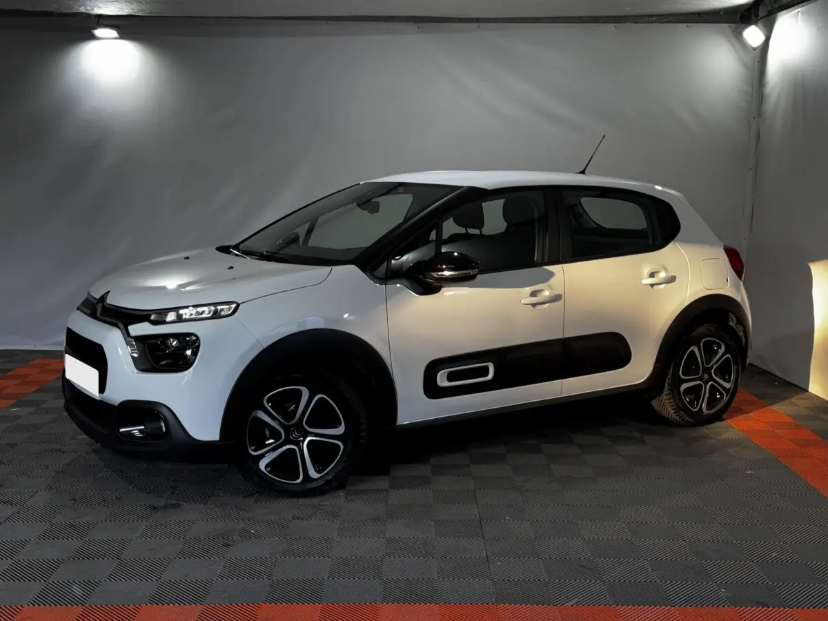 Citroën C3 blanche vue de profil droit en intérieur, avec protections latérales noires et jantes stylisées.