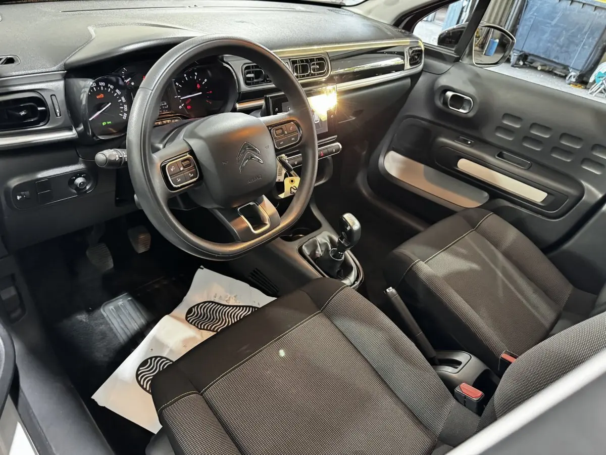 Intérieur de la Citroën C3 2024 vu côté conducteur, volant multifonctions, tableau de bord noir et sièges tissu gris.