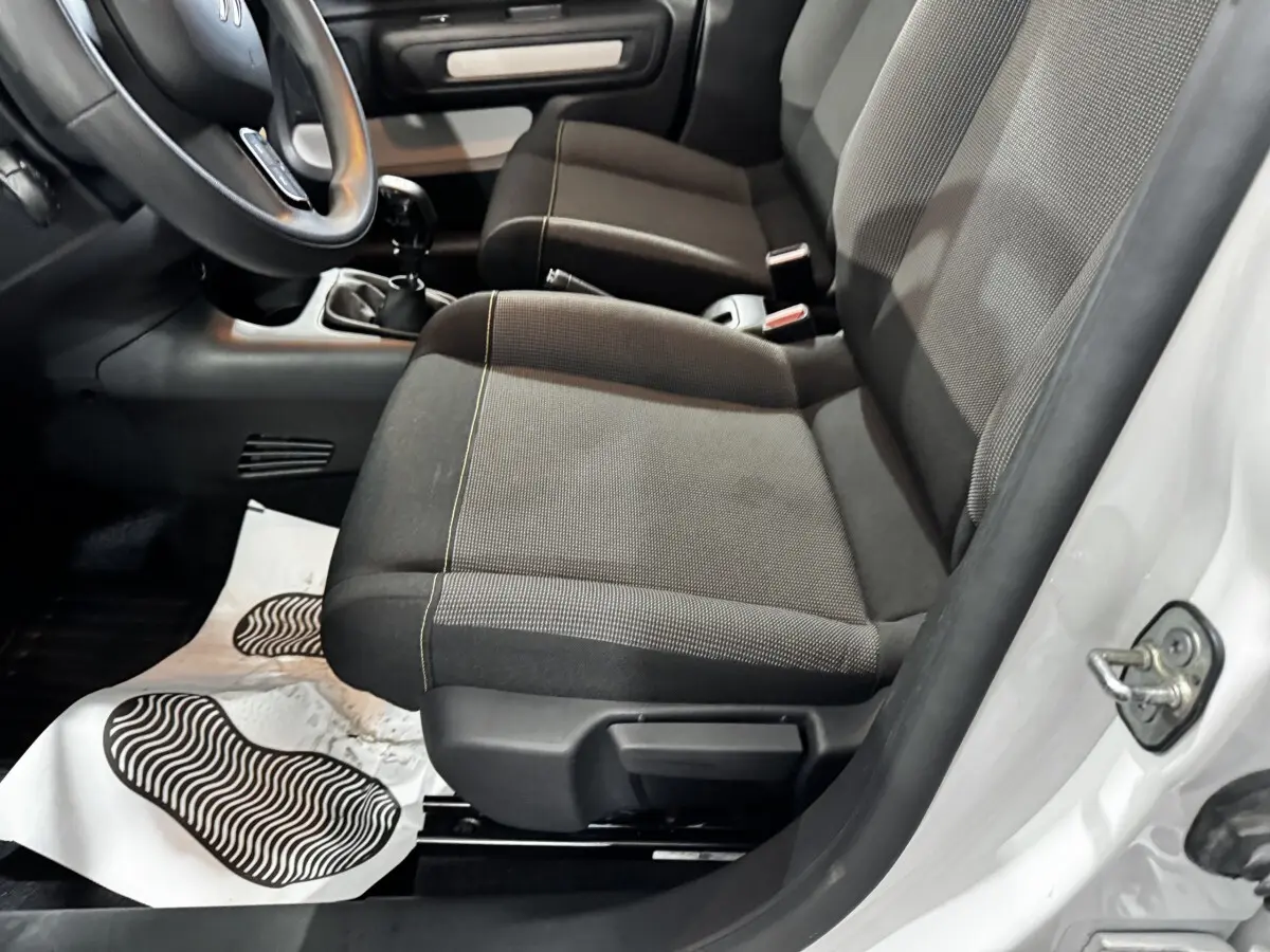 Vue intérieure côté conducteur de la Citroën C3 blanche 2024, montrant les sièges avant en tissu gris et la boîte manuelle.