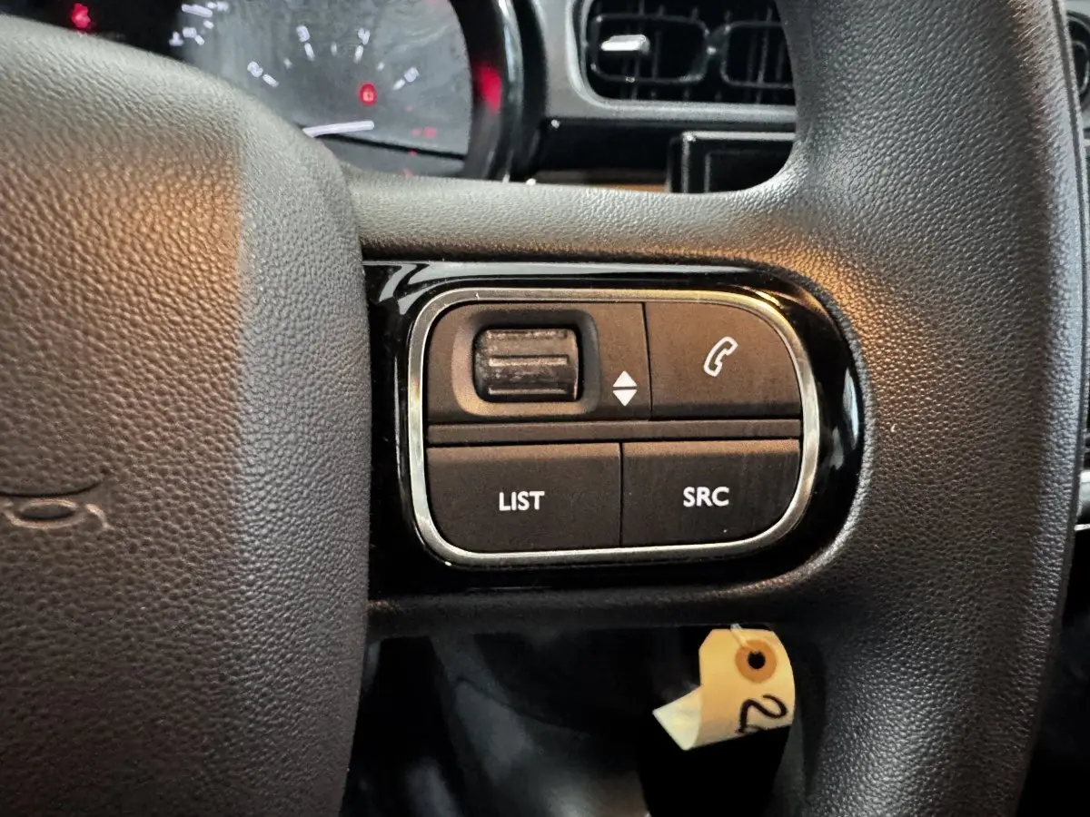 Gros plan sur les commandes multifonctions du volant noir d’une Citroën C3 PureTech 2024, intérieur sombre.