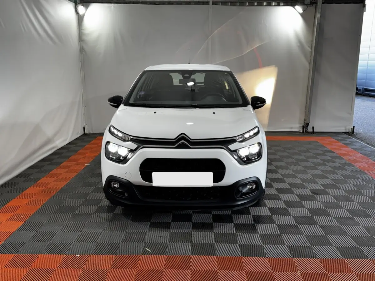 Vue frontale d'une Citroën C3 blanche 2024 avec phares LED allumés dans un garage éclairé.
