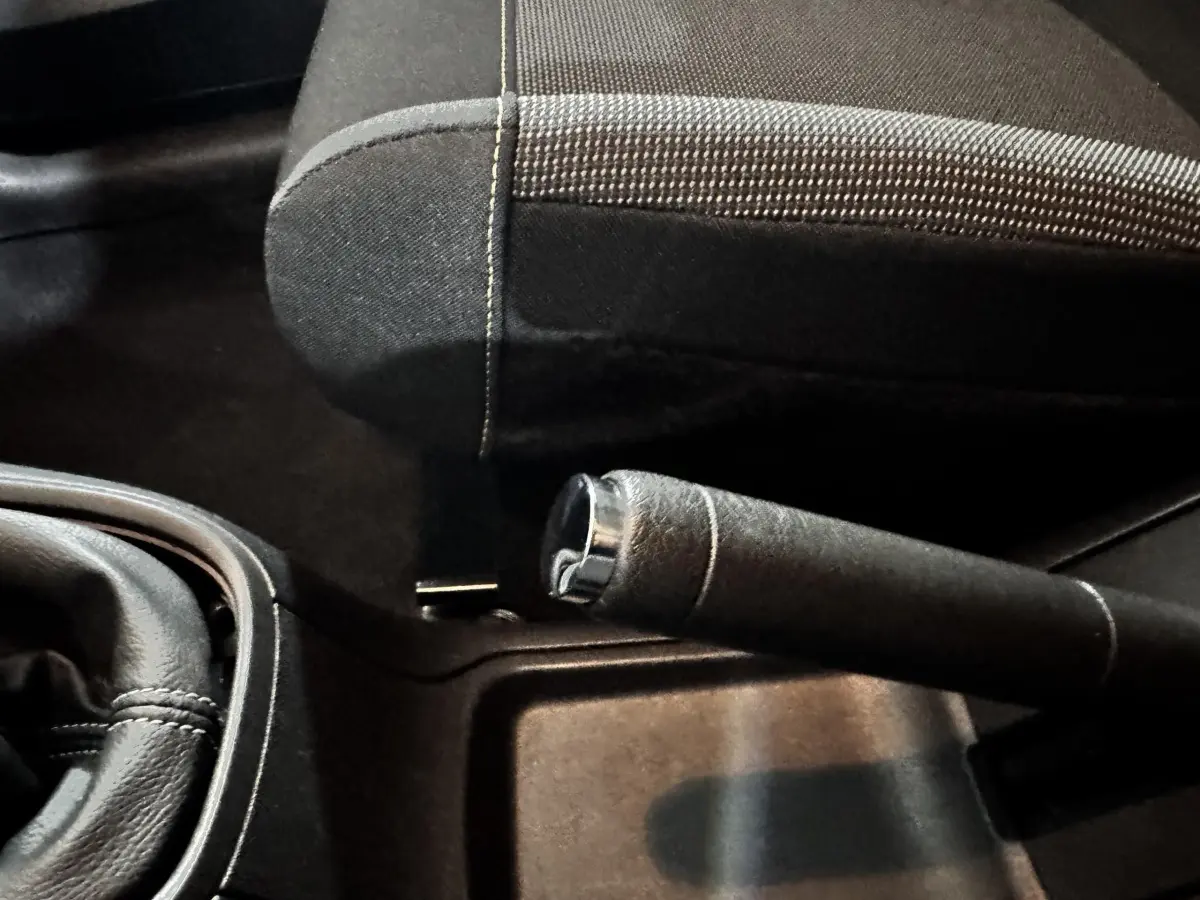 Gros plan sur le frein à main et le siège avant en tissu noir de la Citroën C3 PureTech 83 blanche, intérieur sombre.