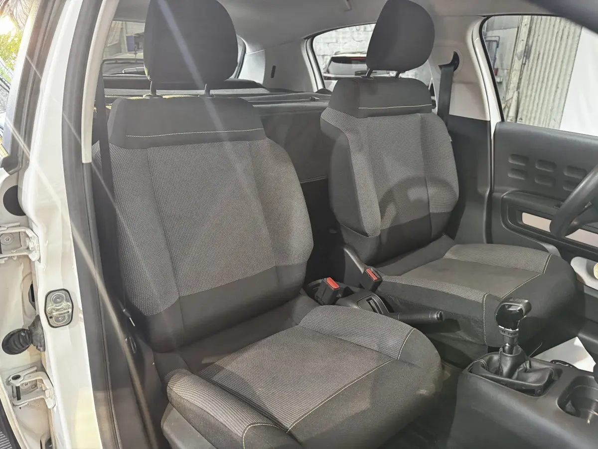 Vue intérieure de face des sièges avant gris foncé de la Citroën C3 blanche, avec levier de vitesse manuel visible.
