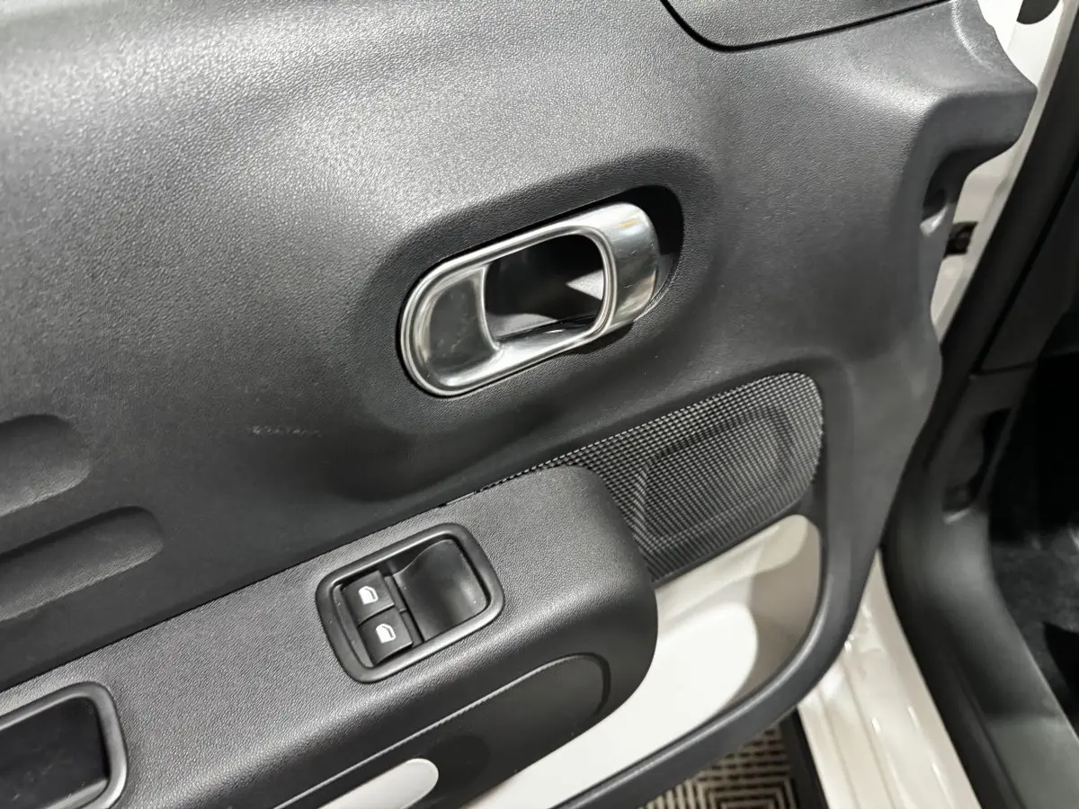 Gros plan sur la porte avant droite blanche d’une Citroën C3 2024, avec poignée intérieure chromée et commandes de vitres.