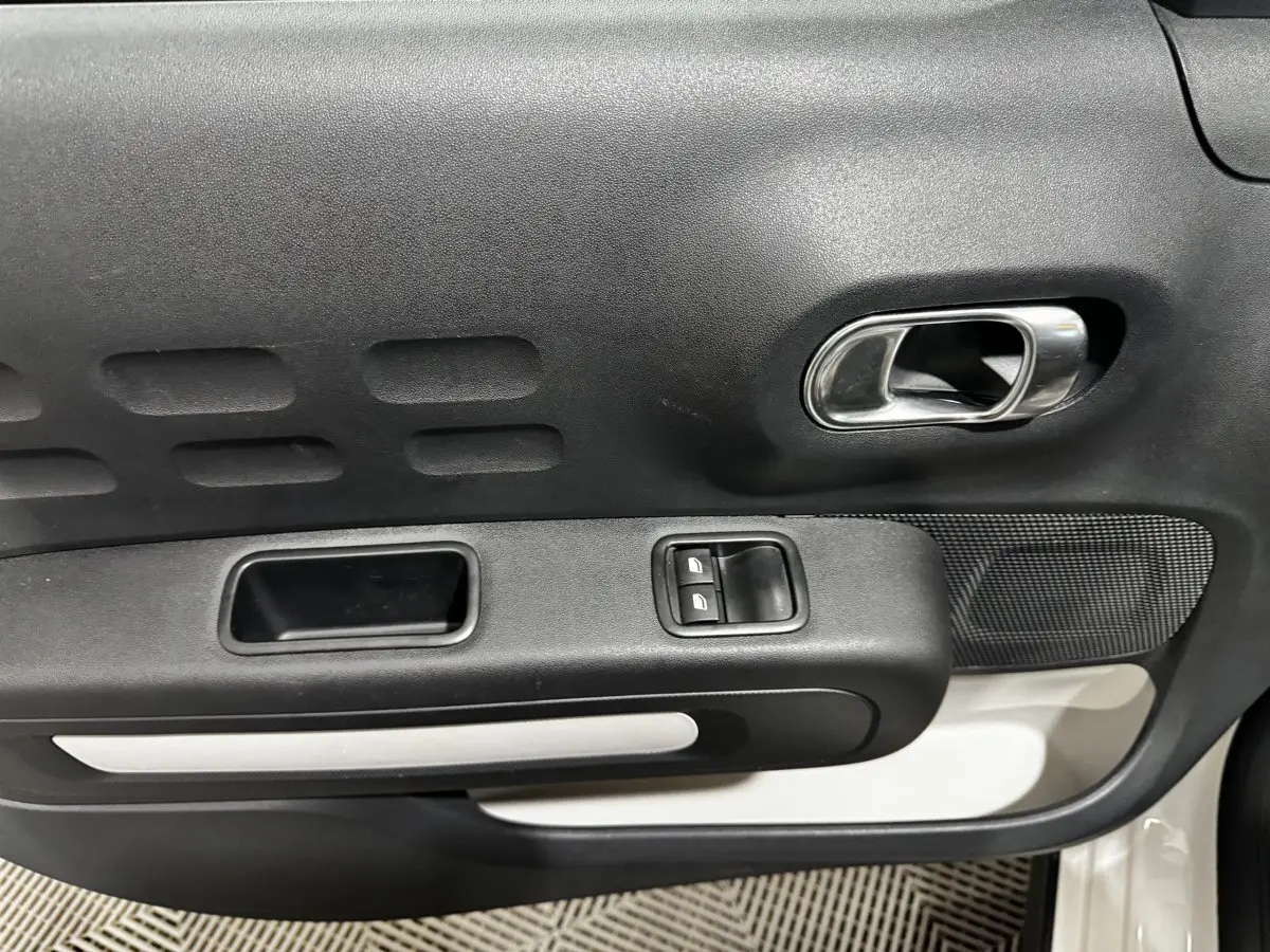 Détail de la porte intérieure côté conducteur de la Citroën C3 blanche 2024 avec commandes de vitres et poignée chromée.
