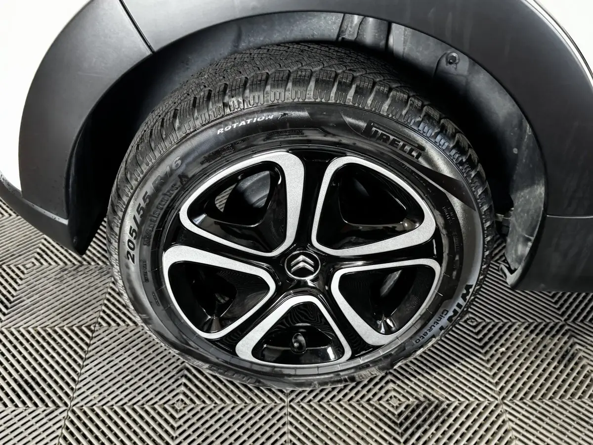 Gros plan sur la roue avant droite d'une Citroën C3 blanche, jante alliage noire et argent avec logo Citroën central.