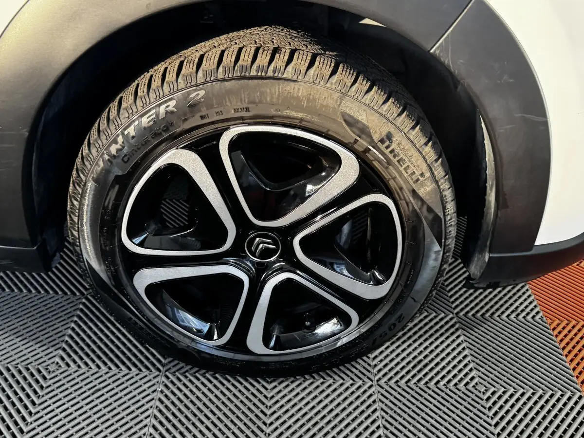 Gros plan sur la roue avant droite d'une Citroën C3 blanche, mettant en valeur la jante noire et argentée au design moderne.