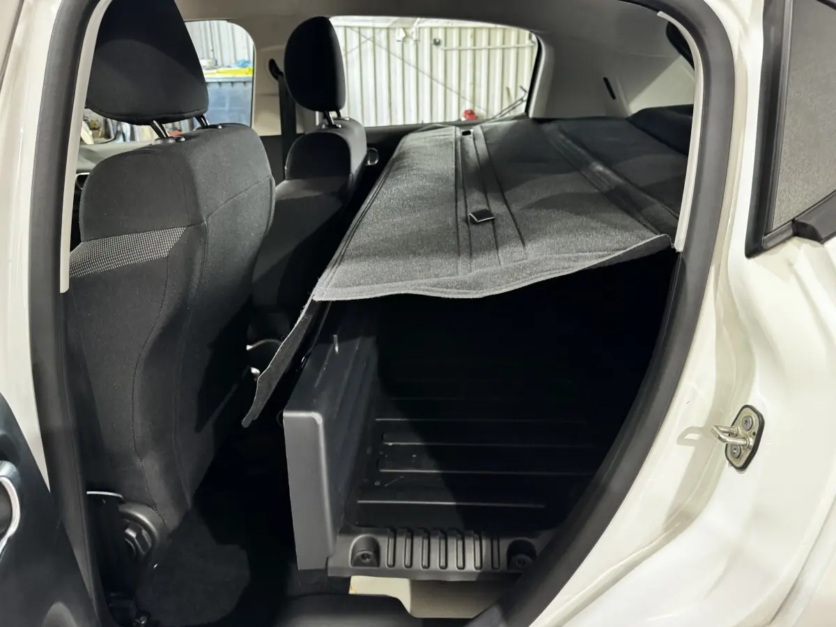Vue intérieure arrière côté droit d'une Citroën C3 blanche 2024, coffre ouvert avec cache-bagages partiellement relevé.