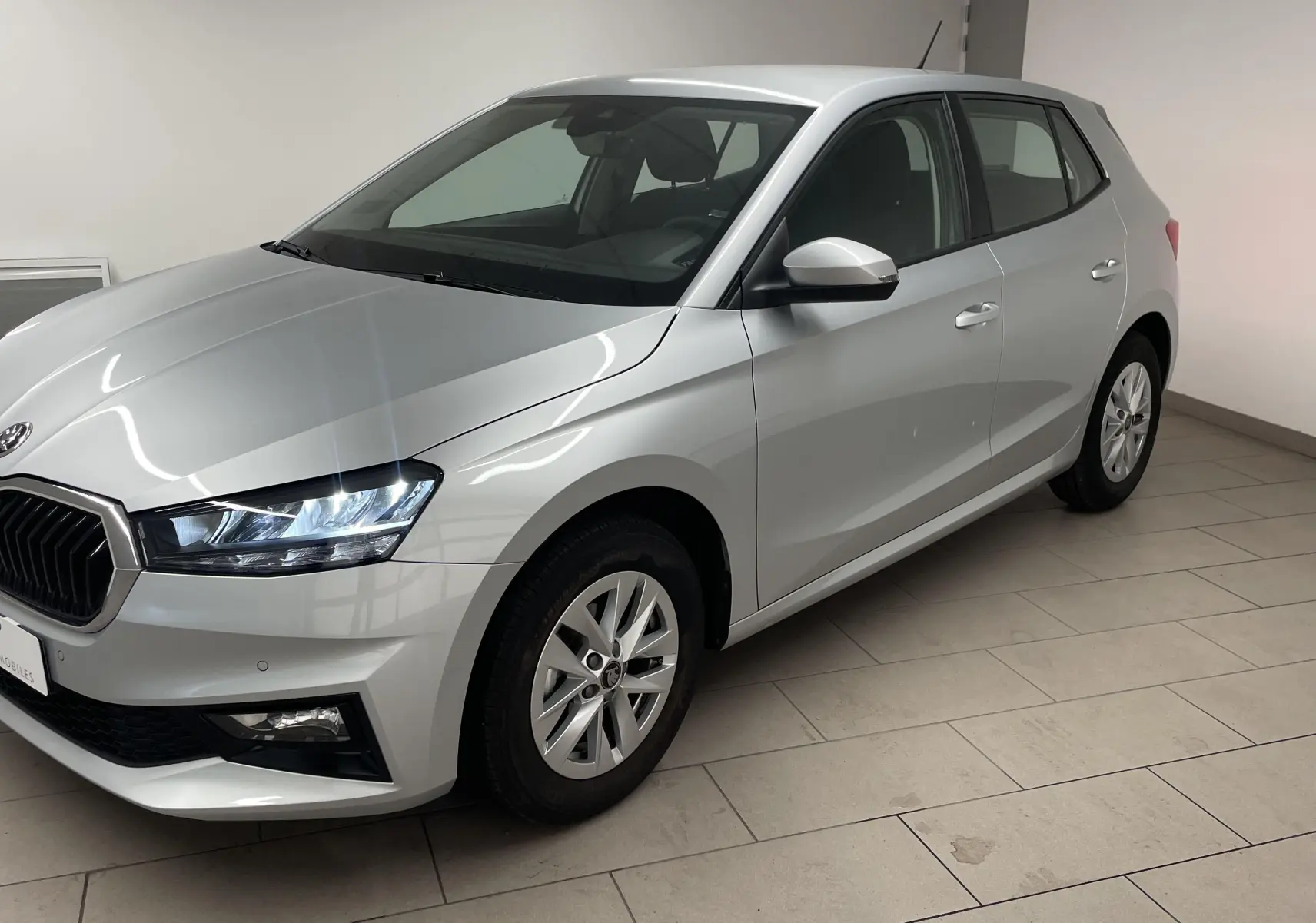 SKODA FABIA 2025 gris argent vue 3/4 avant droit dans un intérieur clair avec calandre noire distinctive.