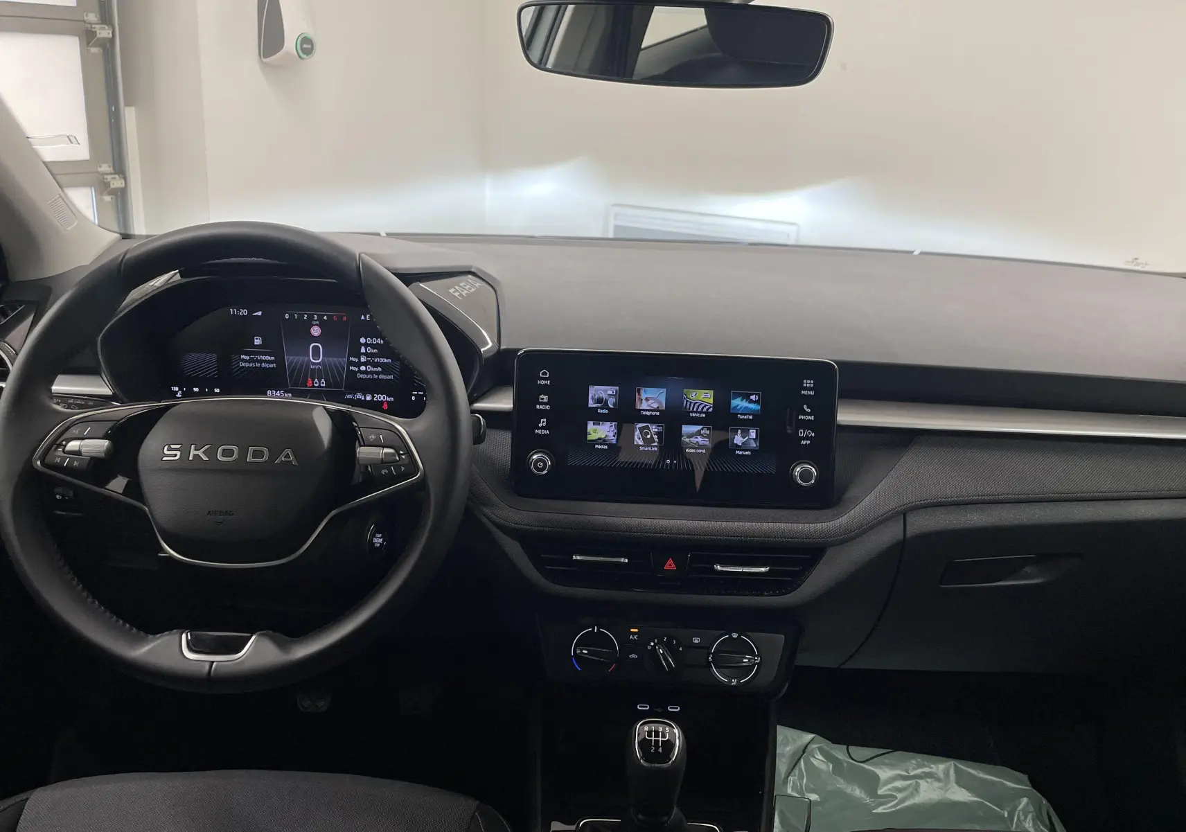 Vue frontale de l'habitacle de la Skoda Fabia gris argent, avec volant multifonction et écran tactile central allumé.