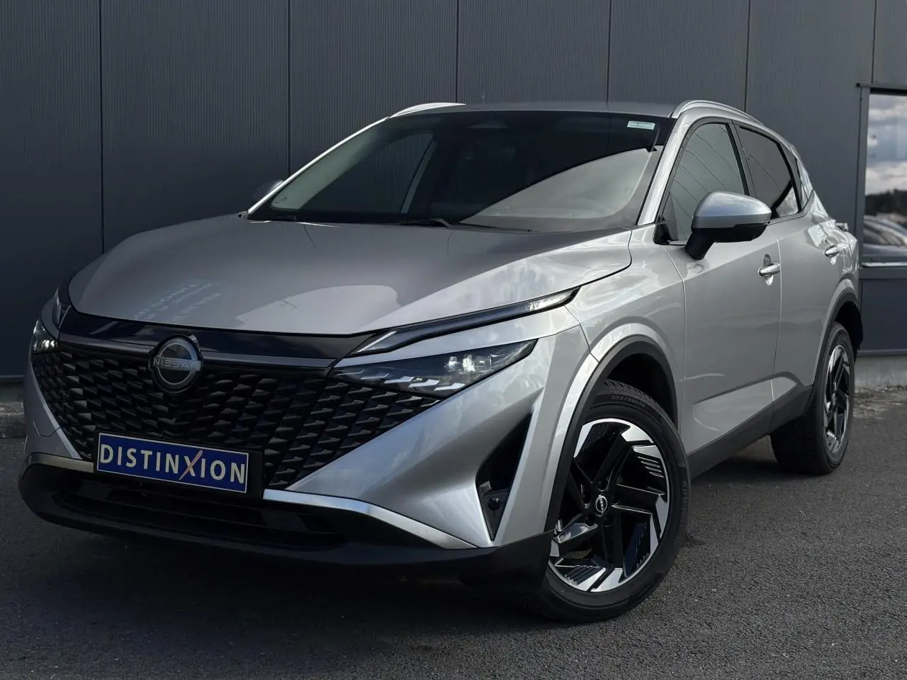 Nissan Qashqai 2024 gris métallisé en 3/4 avant droit avec calandre noire et jantes alliage noires.