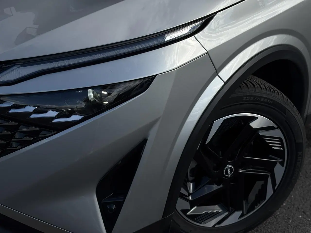 Gros plan sur l'avant droit du Nissan Qashqai 2024 gris foncé, mettant en valeur le phare LED et la jante alliage noire.