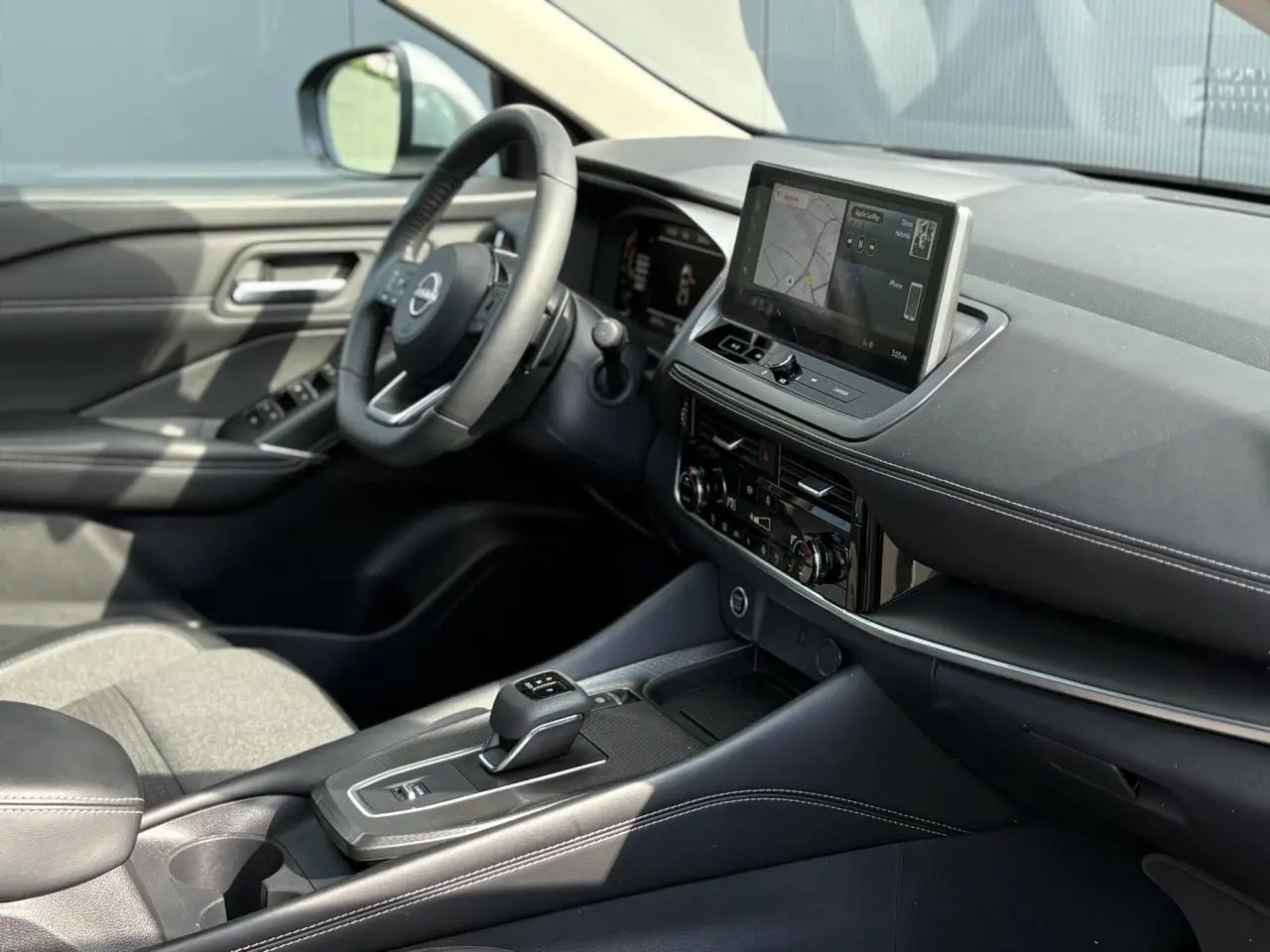 Intérieur du Nissan Qashqai 2024 vu côté conducteur, avec tableau de bord noir et écran tactile central.