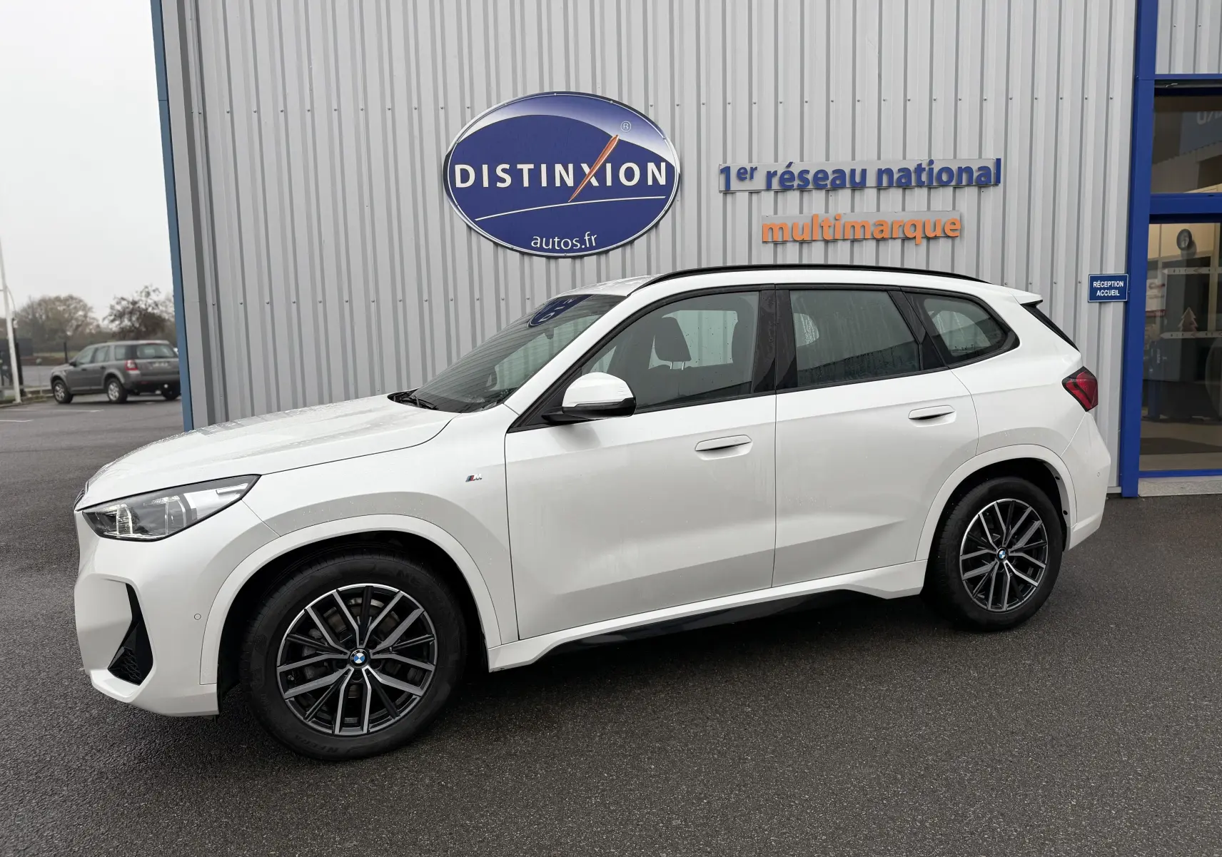 BMW X1 blanc minéral vue de profil côté gauche, avec jantes noires et badge M Sport visible sur aile avant.
